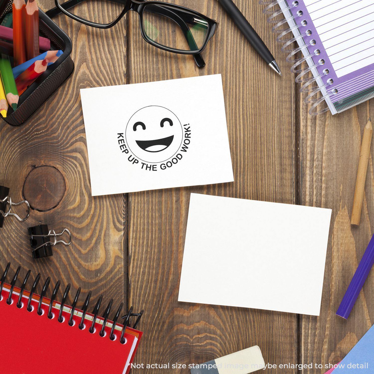 Round Keep up the Good Work Smiley Rubber Stamp on a card, surrounded by office supplies on a wooden desk.