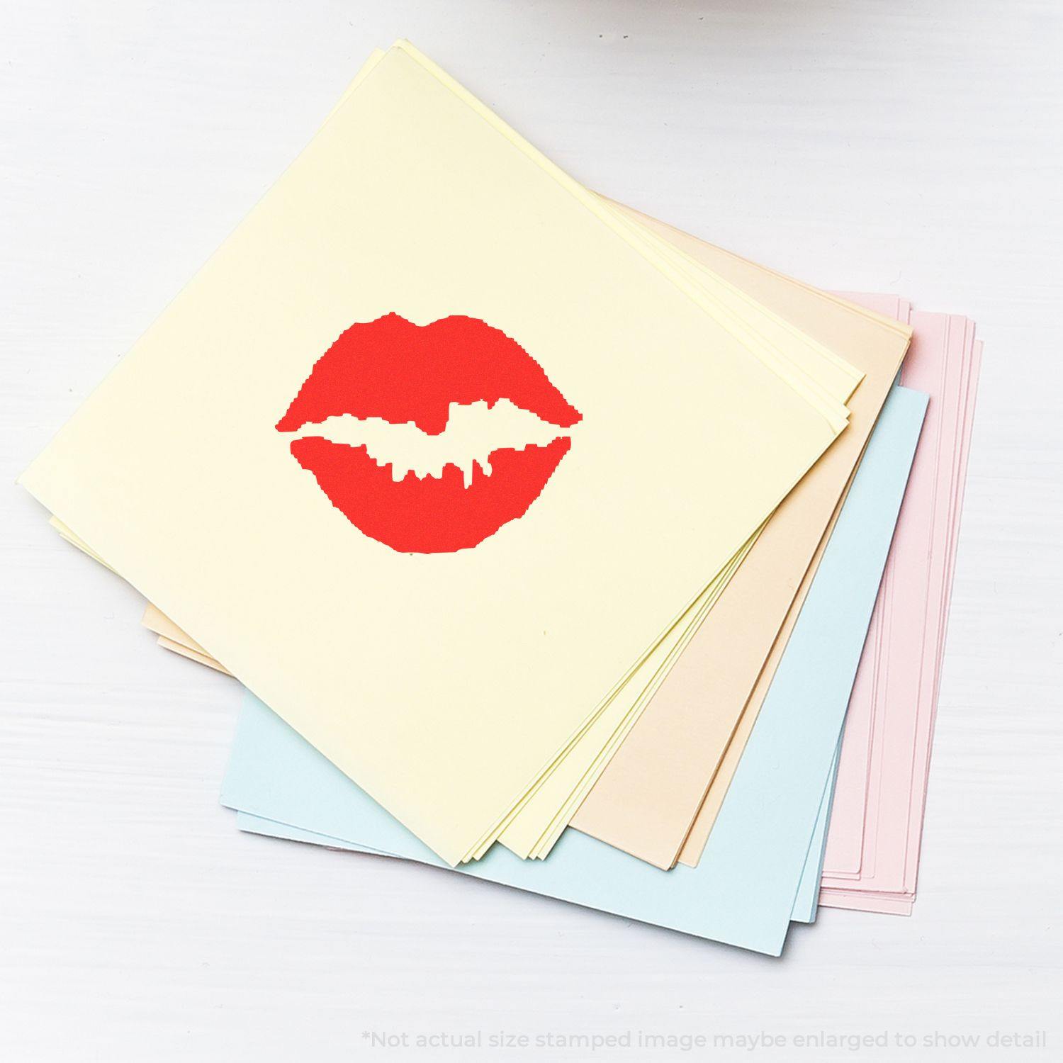 A stack of pastel papers with a red lip print from a round kiss rubber stamp on the top sheet.