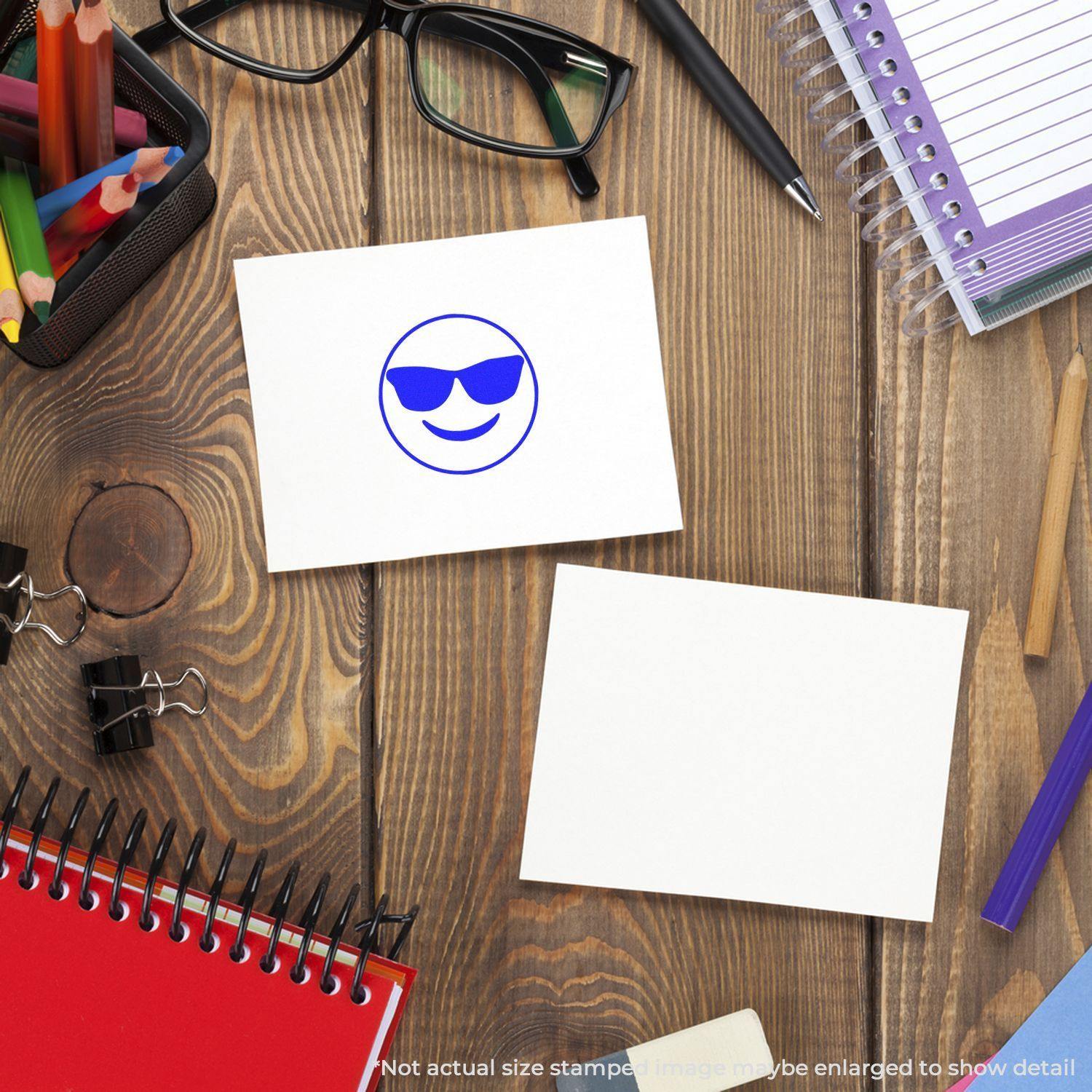 Round Smiley with Sunglasses Rubber Stamp on a white card, surrounded by office supplies on a wooden desk.