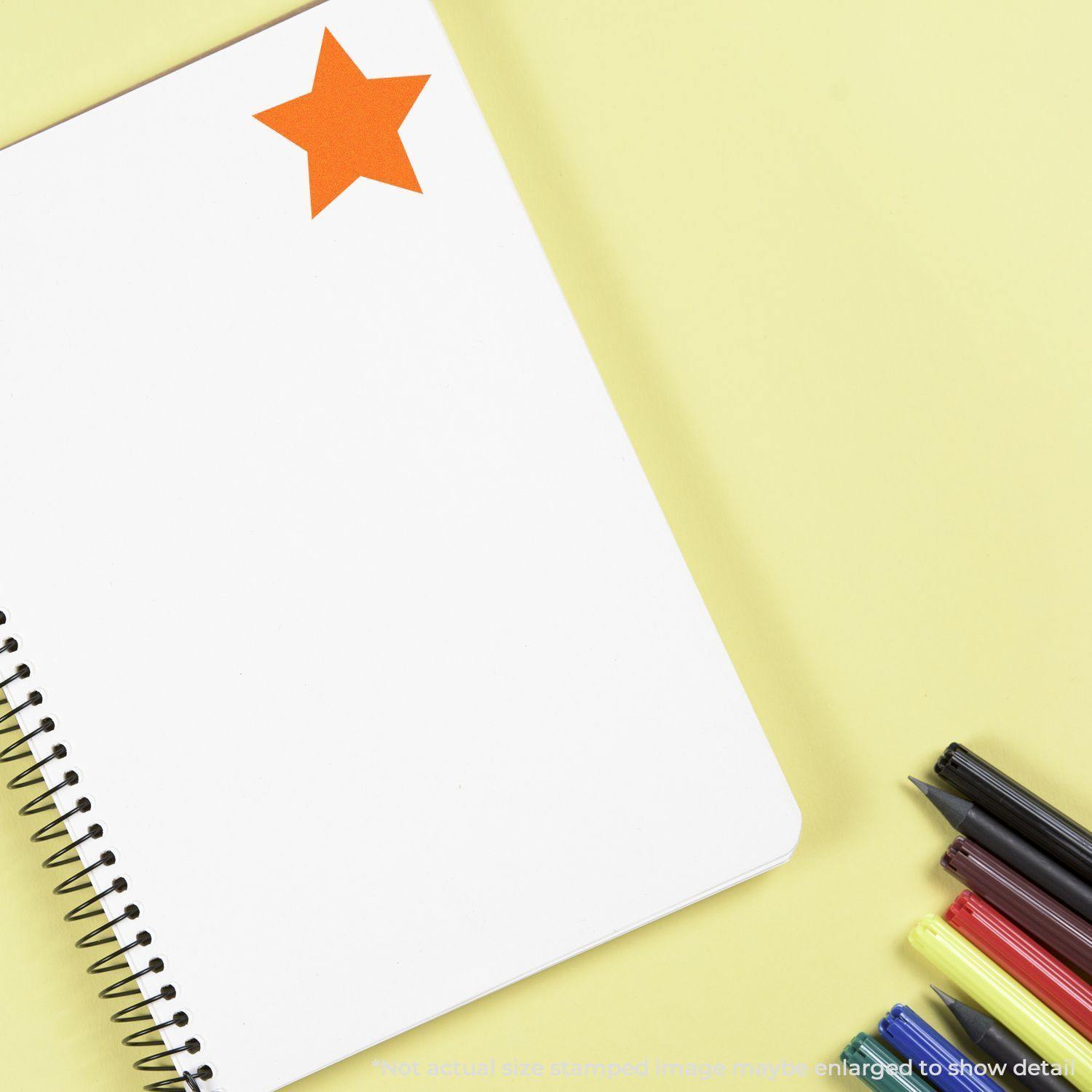 A notebook with an orange Round Solid Star Rubber Stamp on the top left corner, surrounded by colorful markers on a yellow background.