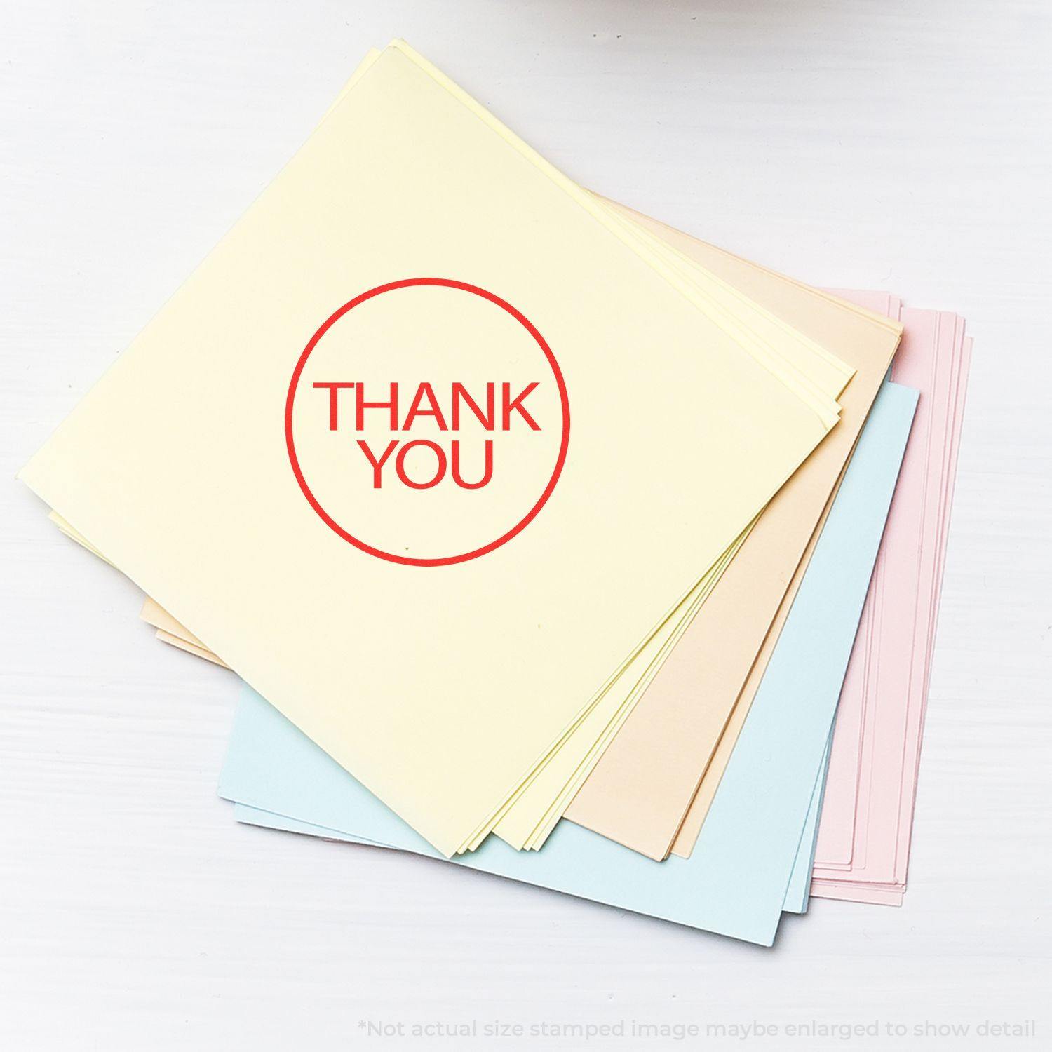 Round Thank You Rubber Stamp on a stack of pastel-colored papers, with the stamped THANK YOU in red prominently displayed.