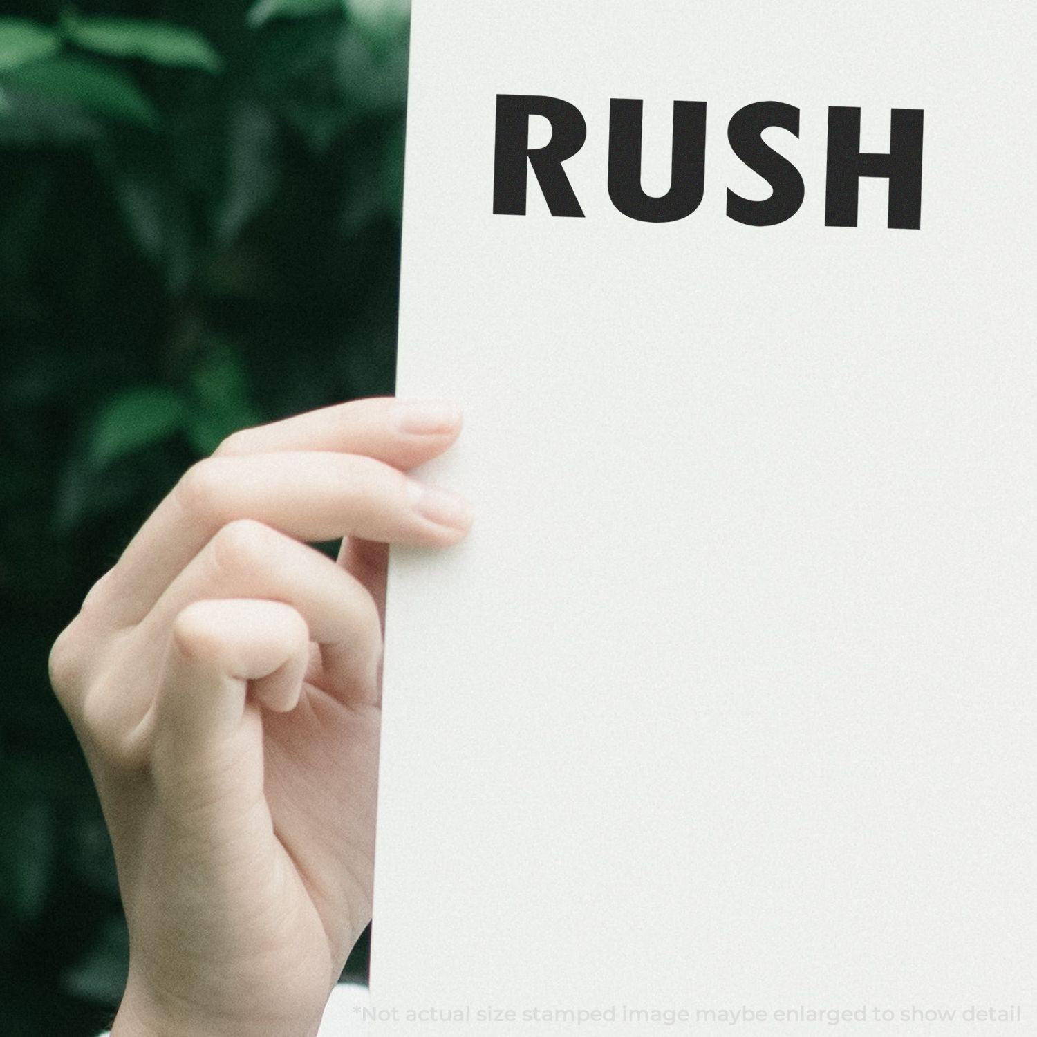 Hand holding a paper stamped with RUSH using a Slim Pre-Inked Rush Stamp, with greenery in the background.