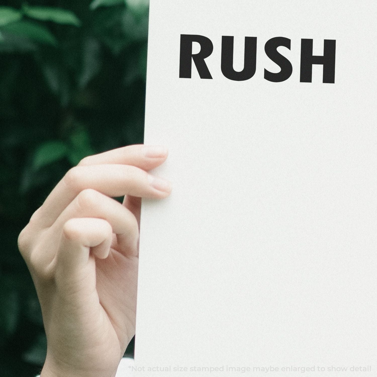 Hand holding a white paper with RUSH stamped in bold black letters using the Self Inking Rush Stamp, greenery in the background.