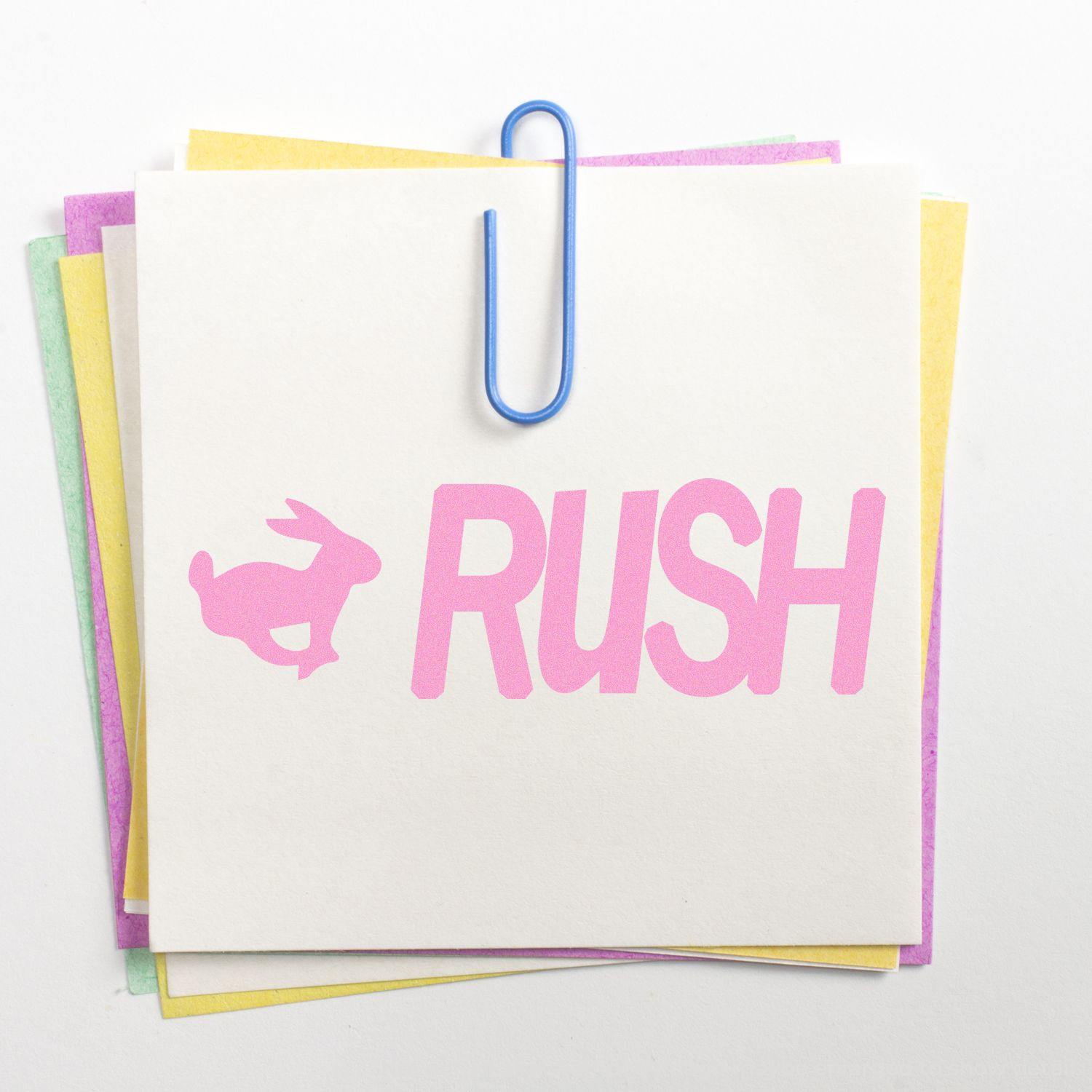 Stack of colorful sticky notes with a blue paperclip, featuring a Slim Pre-Inked Rush with Rabbit Stamp in pink on top note.