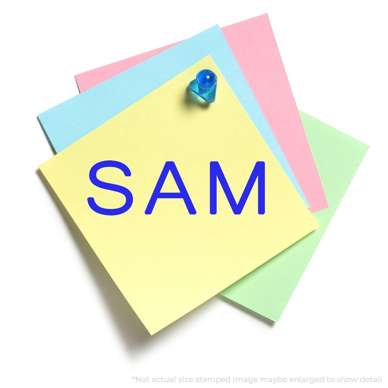 Yellow sticky note with SAM stamped in blue ink, pinned with a blue pushpin on top of pastel-colored papers.