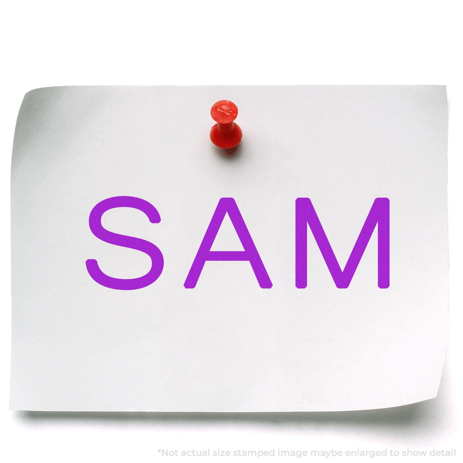 A white paper pinned with a red pushpin displaying the word SAM in purple, stamped using a SAM Rubber Stamp.