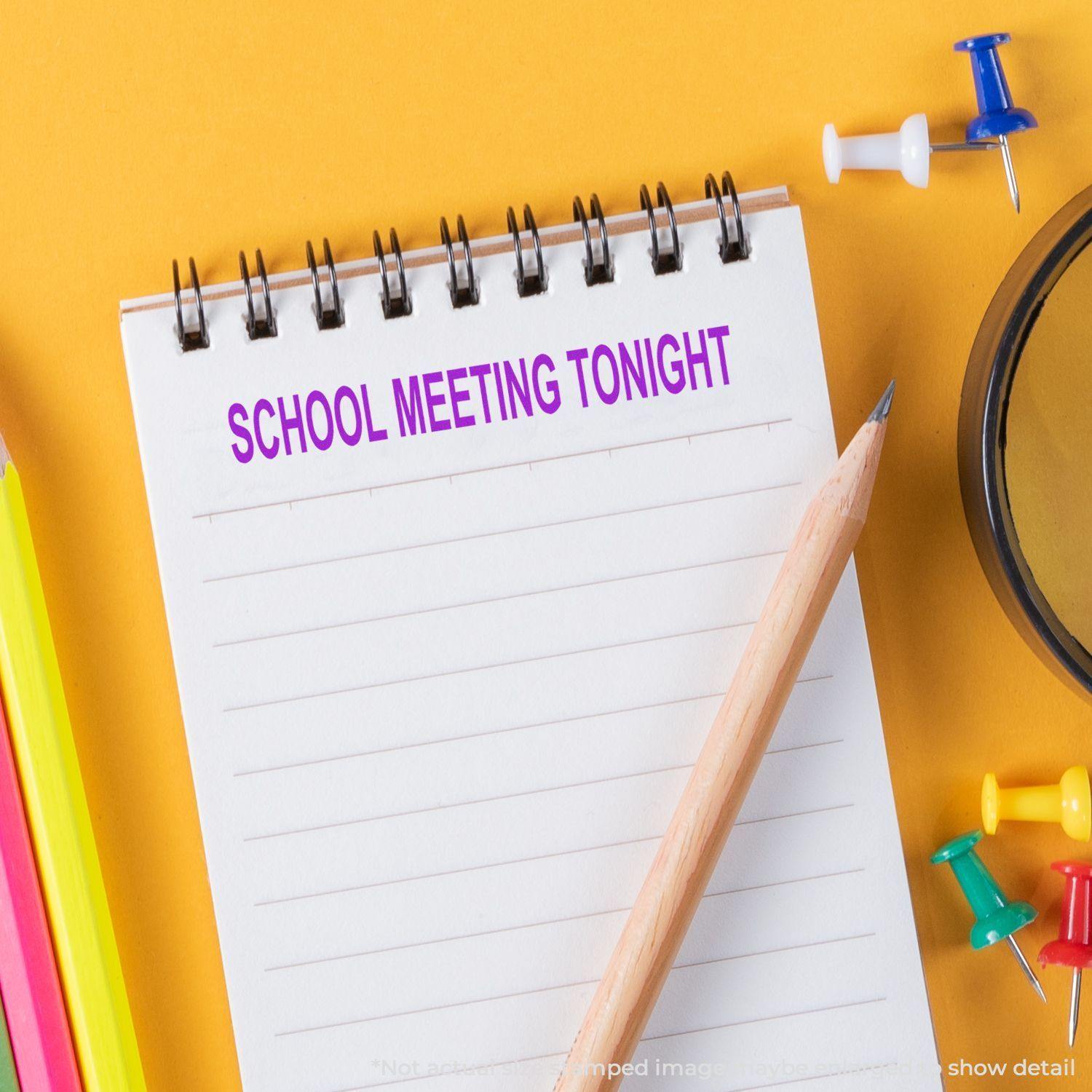 Slim Pre-Inked School Meeting Tonight Stamp on a notepad with a pencil, colorful push pins, and a yellow background.