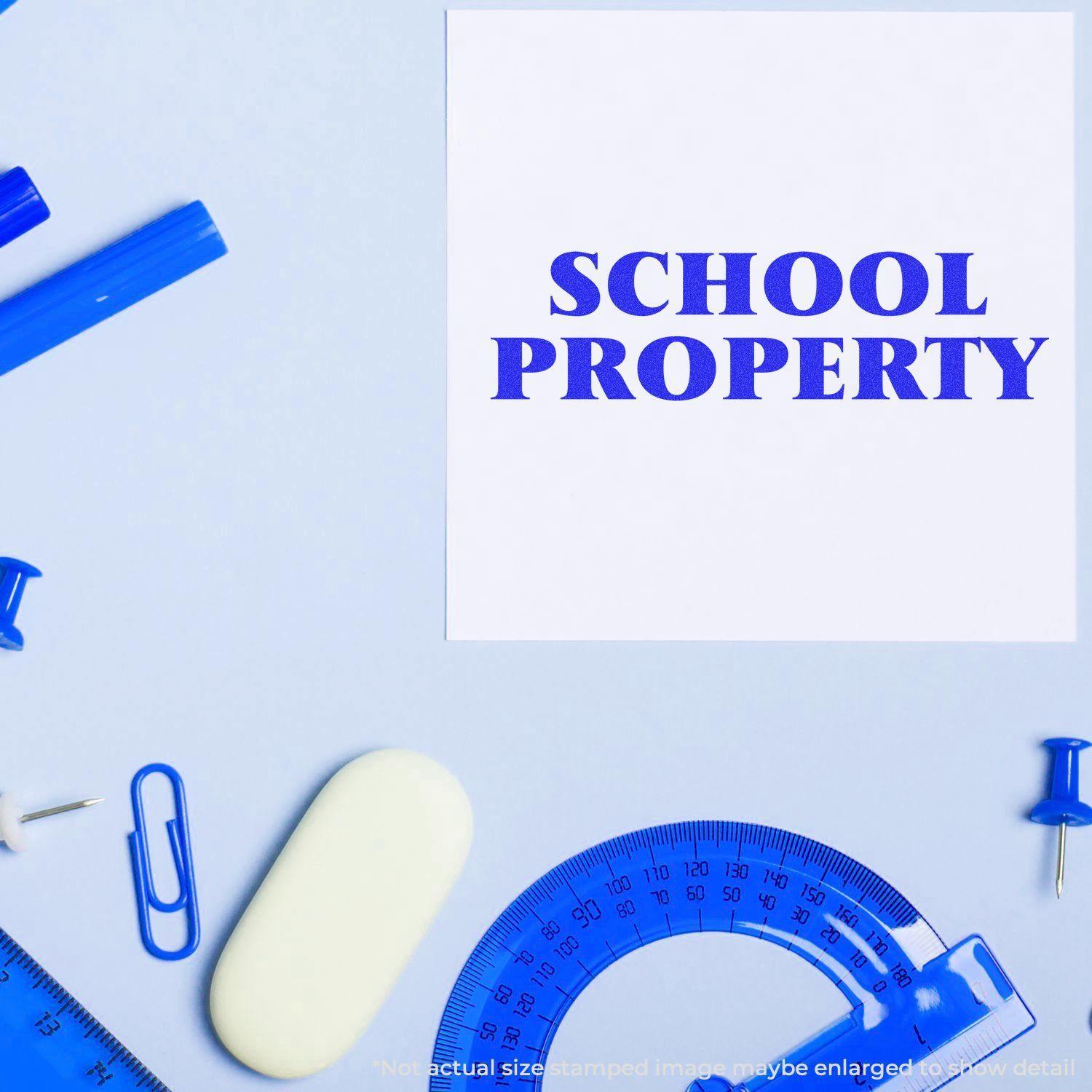 Large Pre-Inked School Property Stamp used on paper, surrounded by blue stationery items like a protractor, pen, and paper clips.