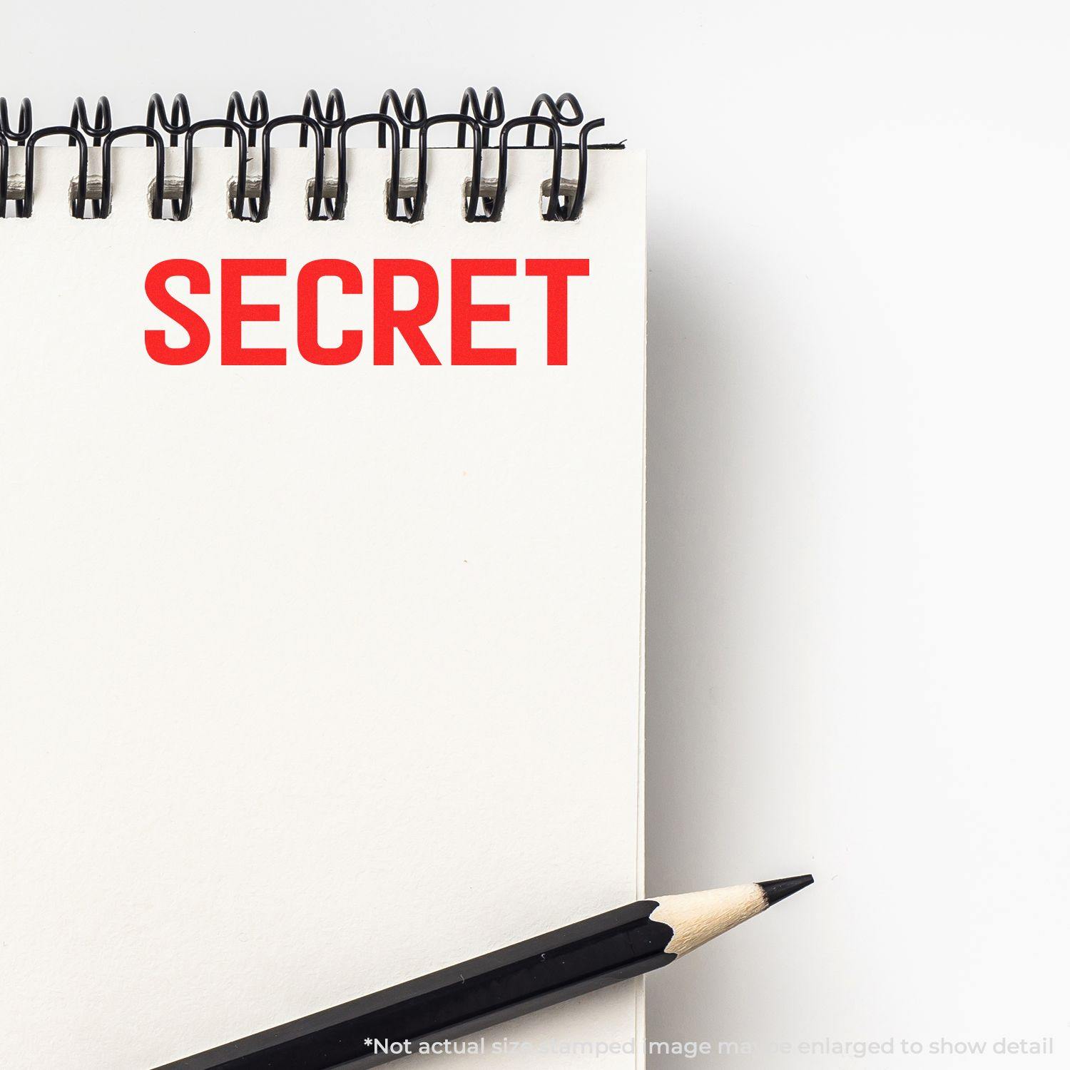 Slim Pre-Inked Secret Stamp marking the word SECRET in red on a white notepad, with a black pencil placed beside it.