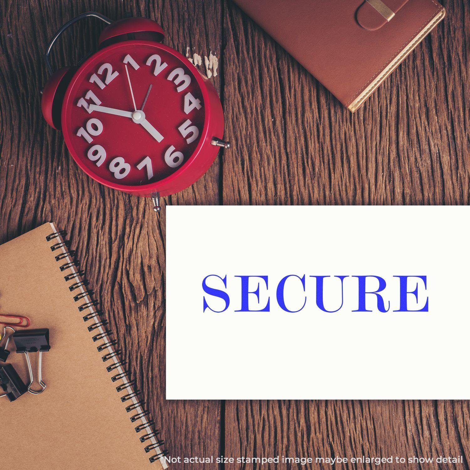 Large Self Inking Secure Stamp used on a white paper, placed on a wooden desk with a red clock, notebook, and office supplies.