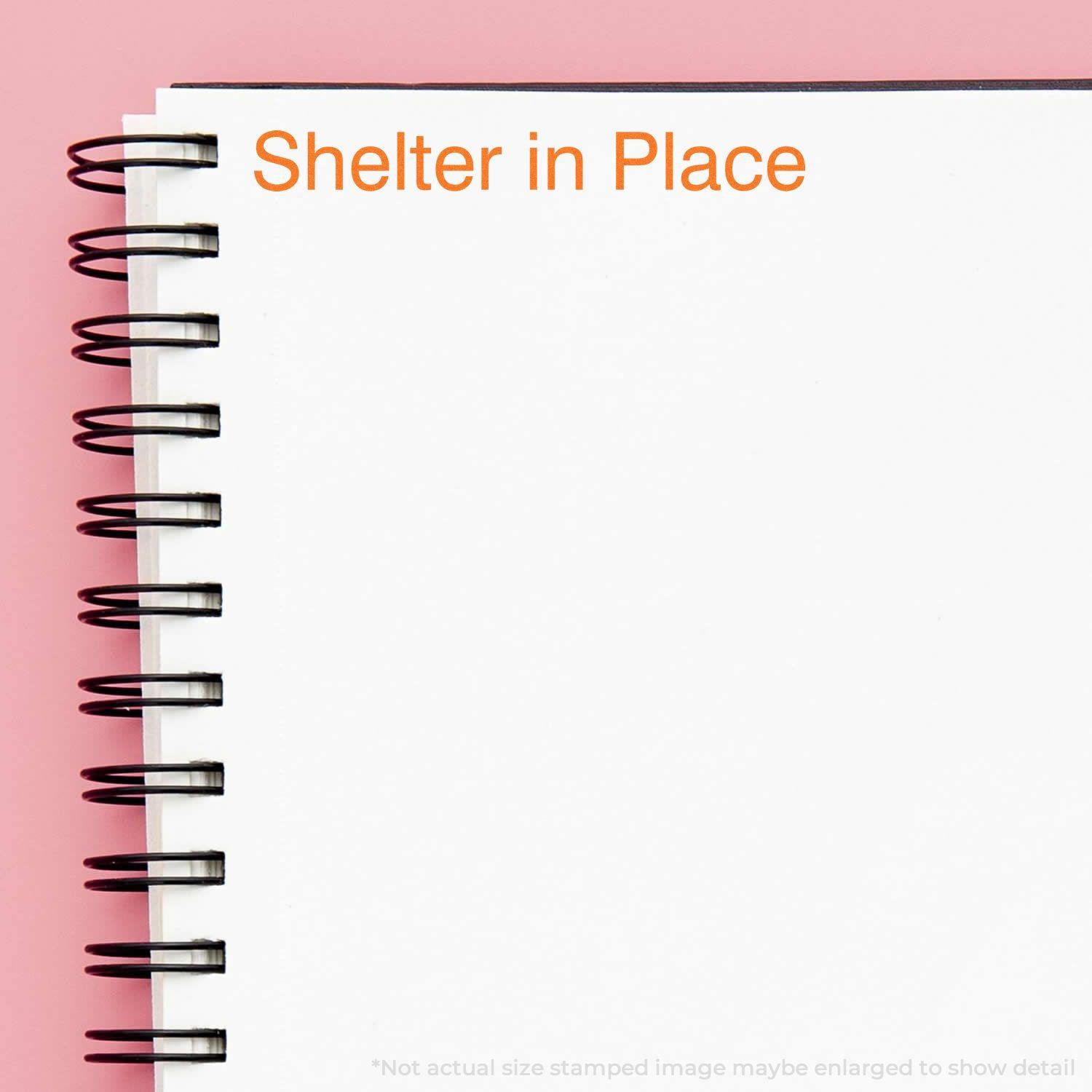 Large Pre-Inked Shelter in Place Stamp used on a white spiral notebook, displaying the text Shelter in Place in orange ink.