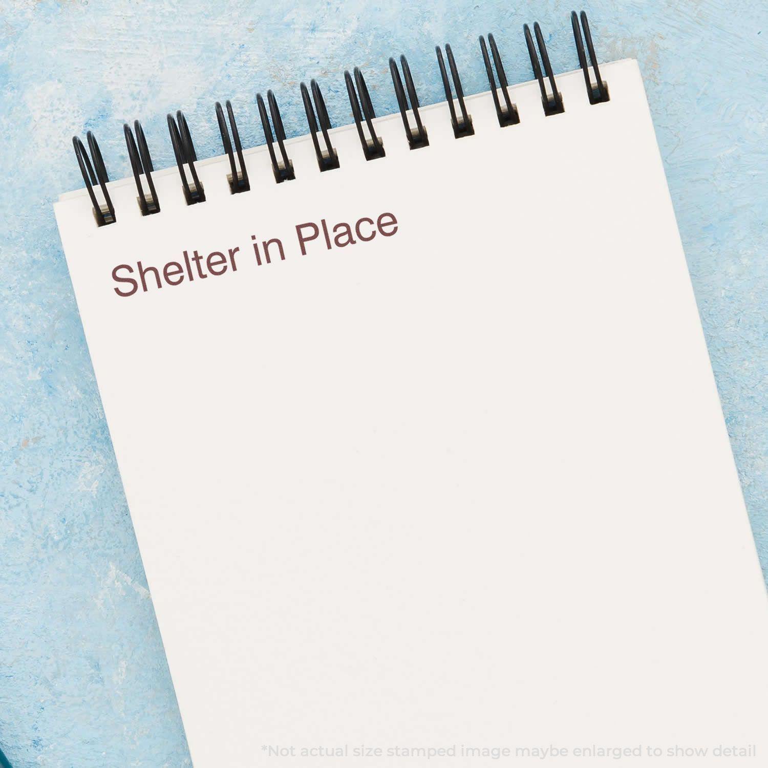 Slim Pre-Inked Shelter in Place Stamp used on a white notepad with a blue background.