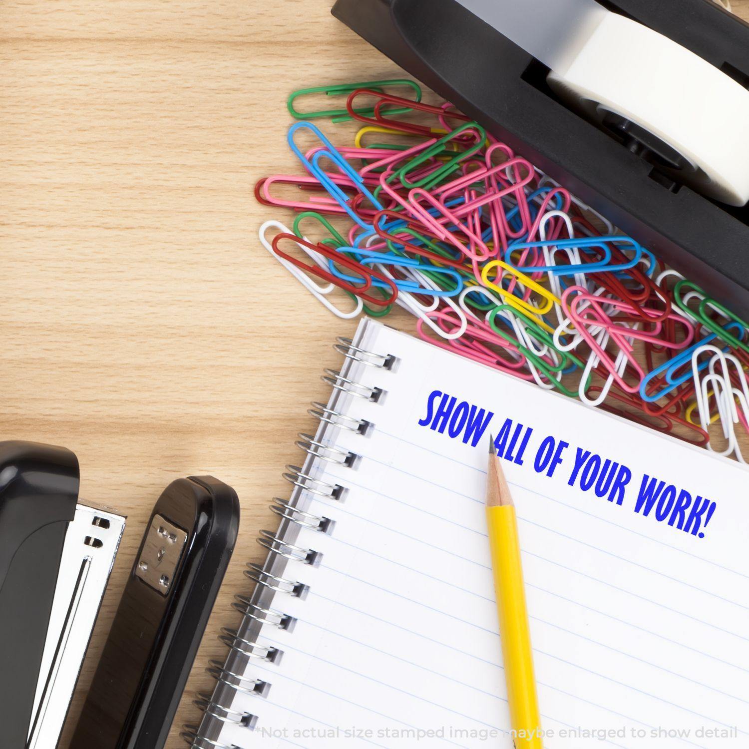 Slim Pre-Inked Show All Of Your Work Stamp used on a notebook page, surrounded by colorful paper clips, stapler, and tape dispenser.