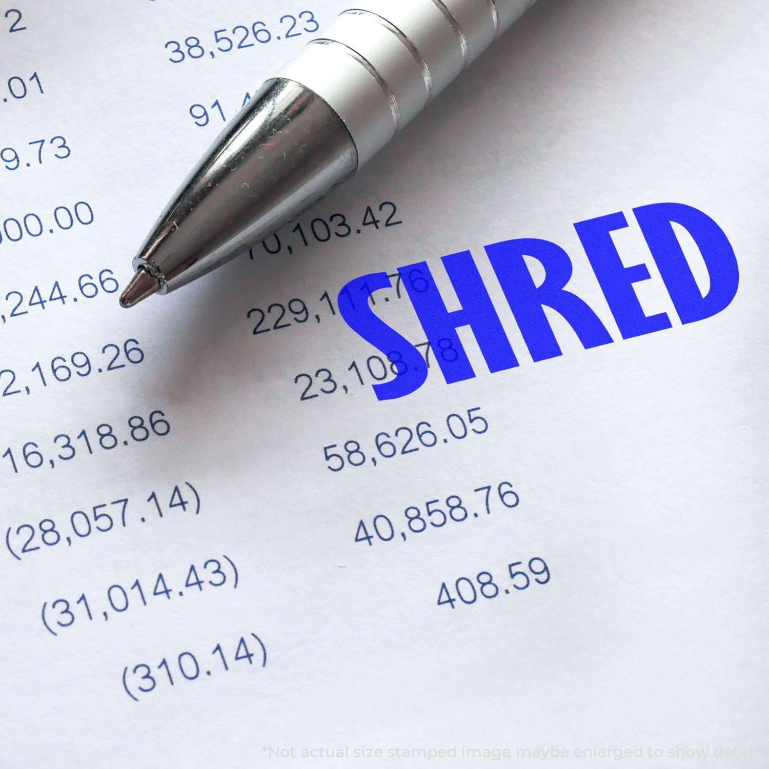 Slim Pre-Inked Shred Stamp in blue ink on a financial document, with a silver pen nearby.