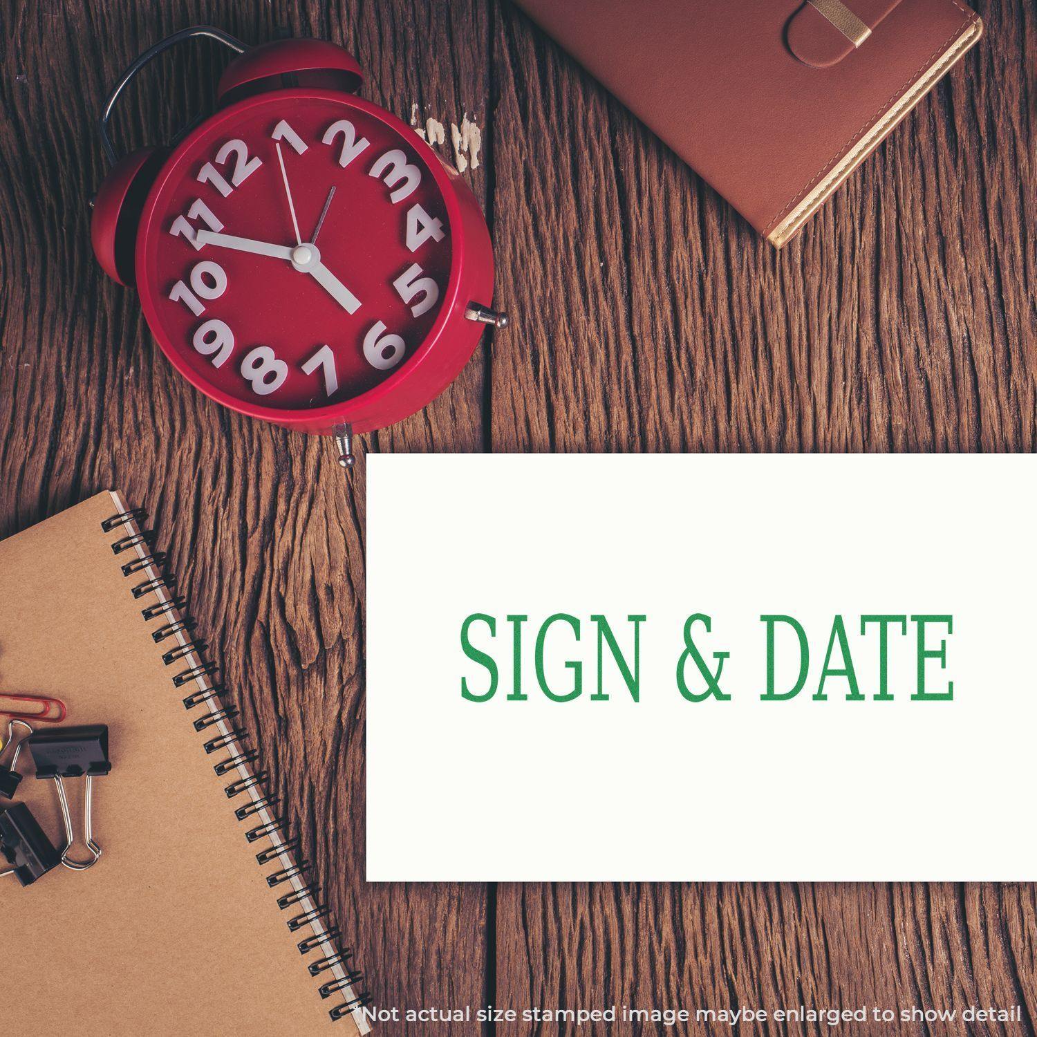 Slim Pre-Inked Sign & Date Stamp used on a white paper, placed on a wooden desk with a red clock, notebook, and office supplies.