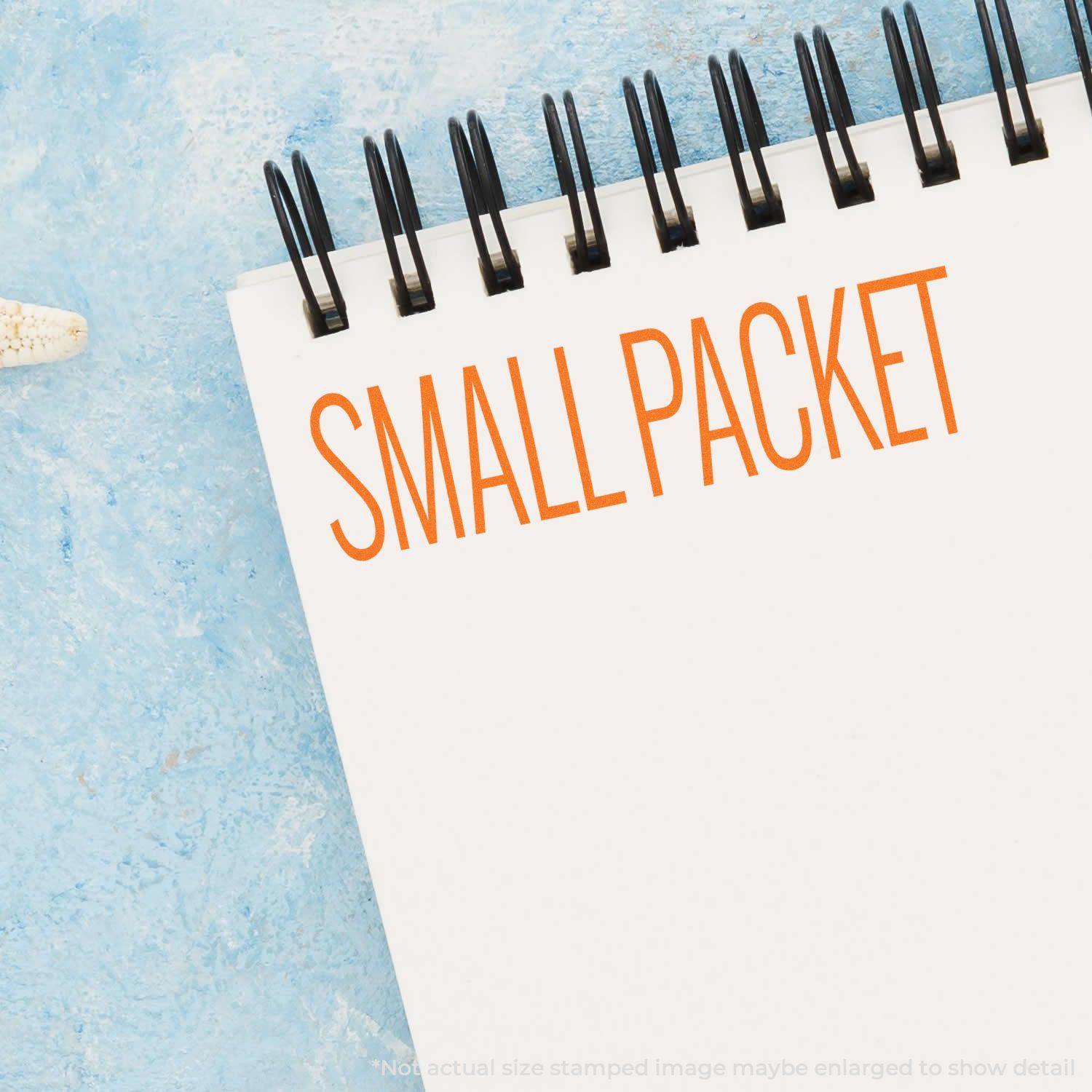 A notebook with SMALL PACKET stamped in orange using the Large Self Inking Small Packet Stamp, placed on a light blue surface.