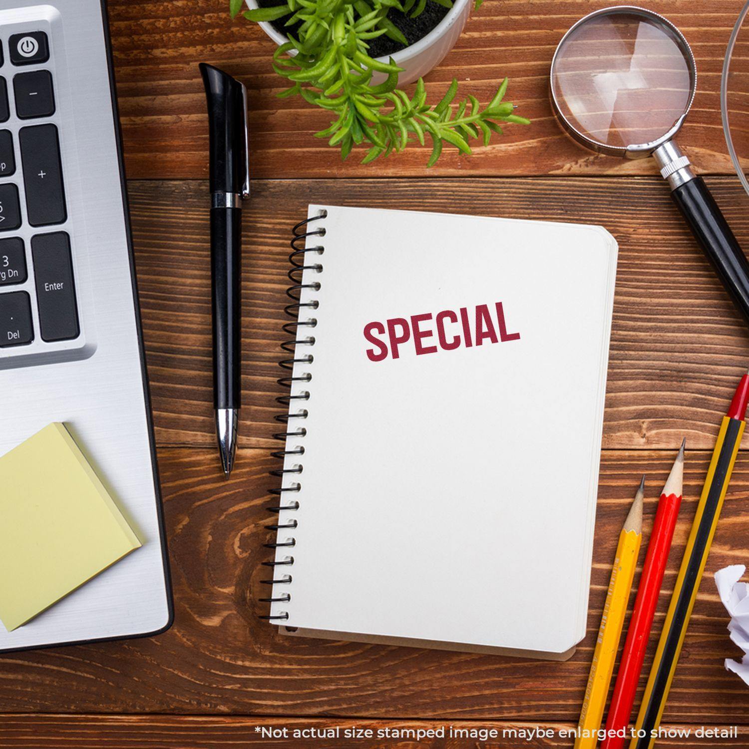 Notebook stamped with SPECIAL using Large Pre-Inked Special Stamp, placed on a wooden desk with laptop, pen, magnifying glass, and pencils.