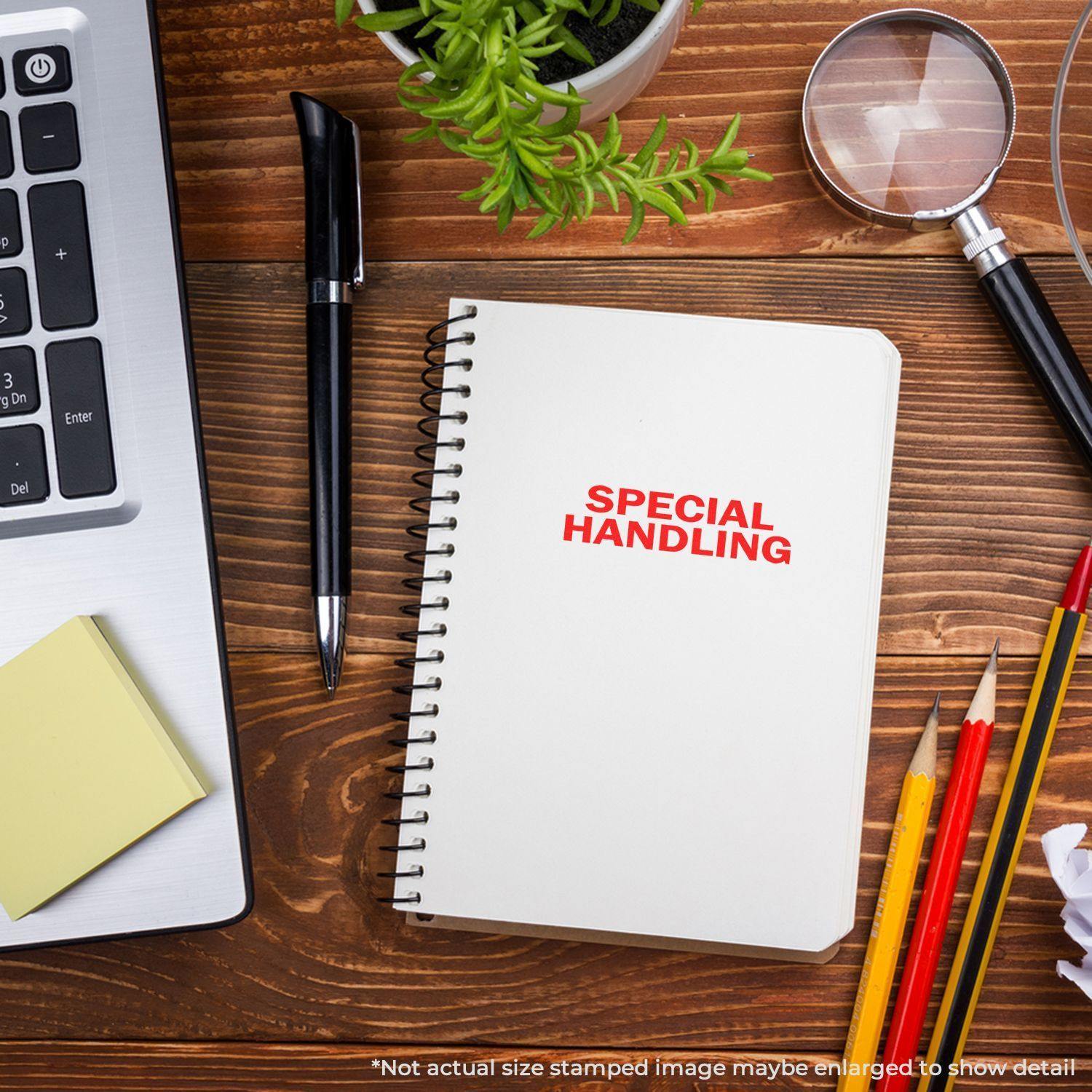 Large Self Inking Special Handling Stamp used on a notebook, placed on a wooden desk with a laptop, plant, magnifying glass, and stationery.