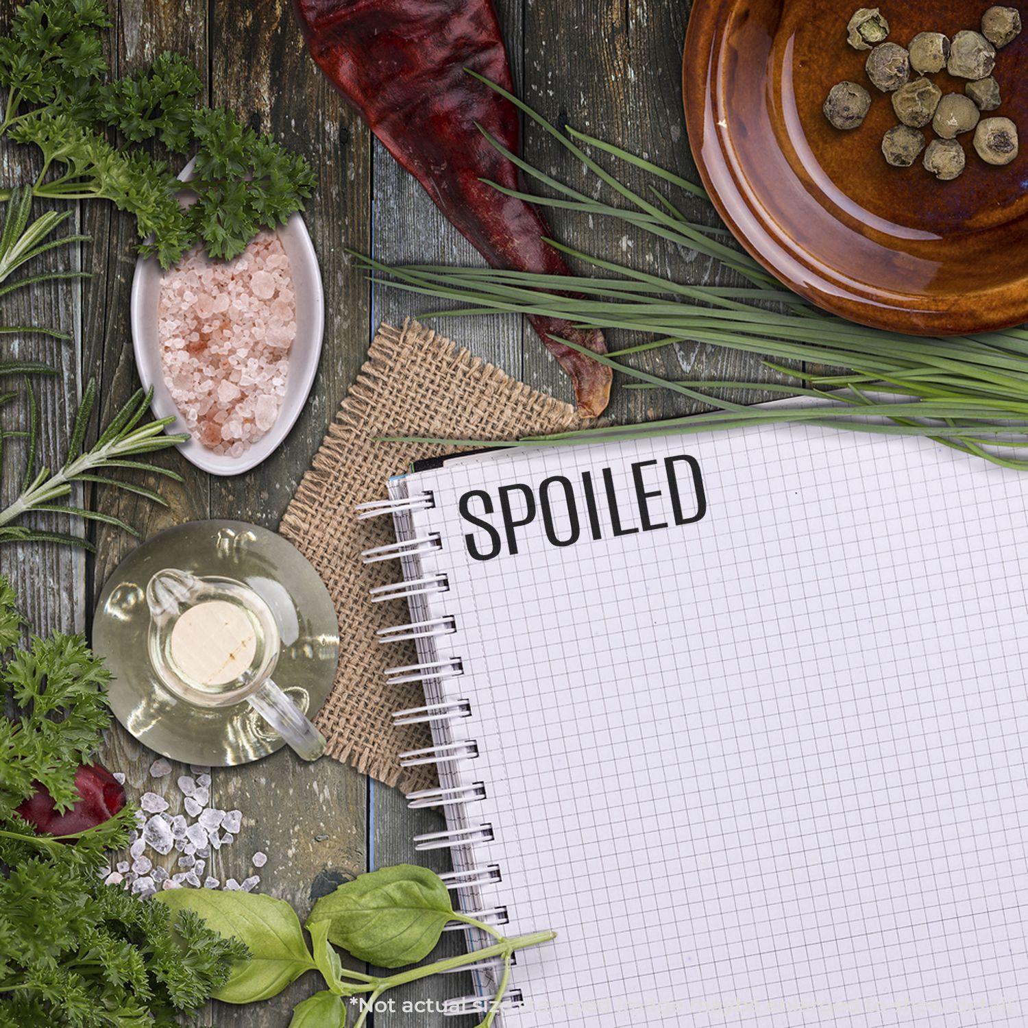 Large Pre-Inked Spoiled Stamp used on a notebook page, surrounded by various herbs, spices, and a red chili pepper on a wooden surface.