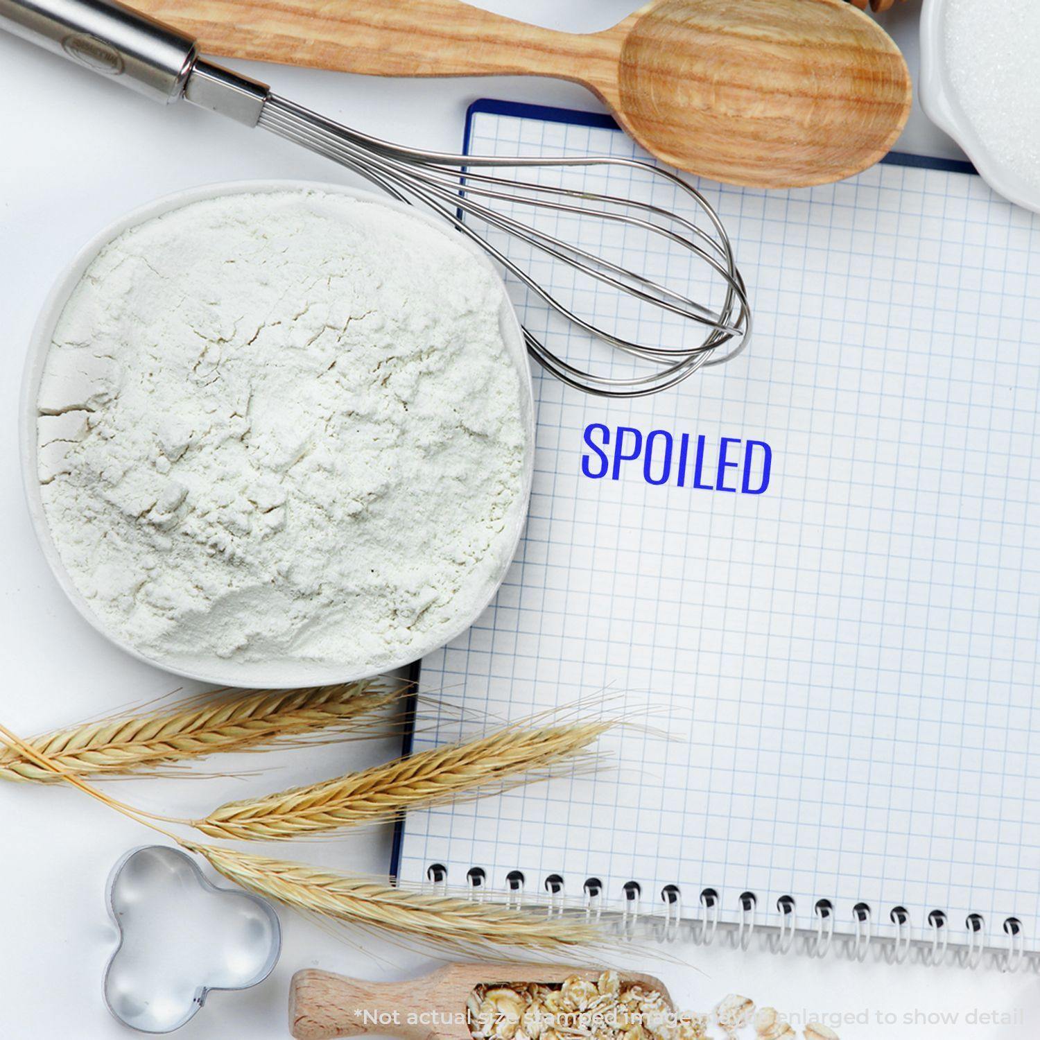 Slim Pre-Inked Spoiled Stamp on a notebook with baking ingredients like flour, whisk, wooden spoon, and wheat around it.