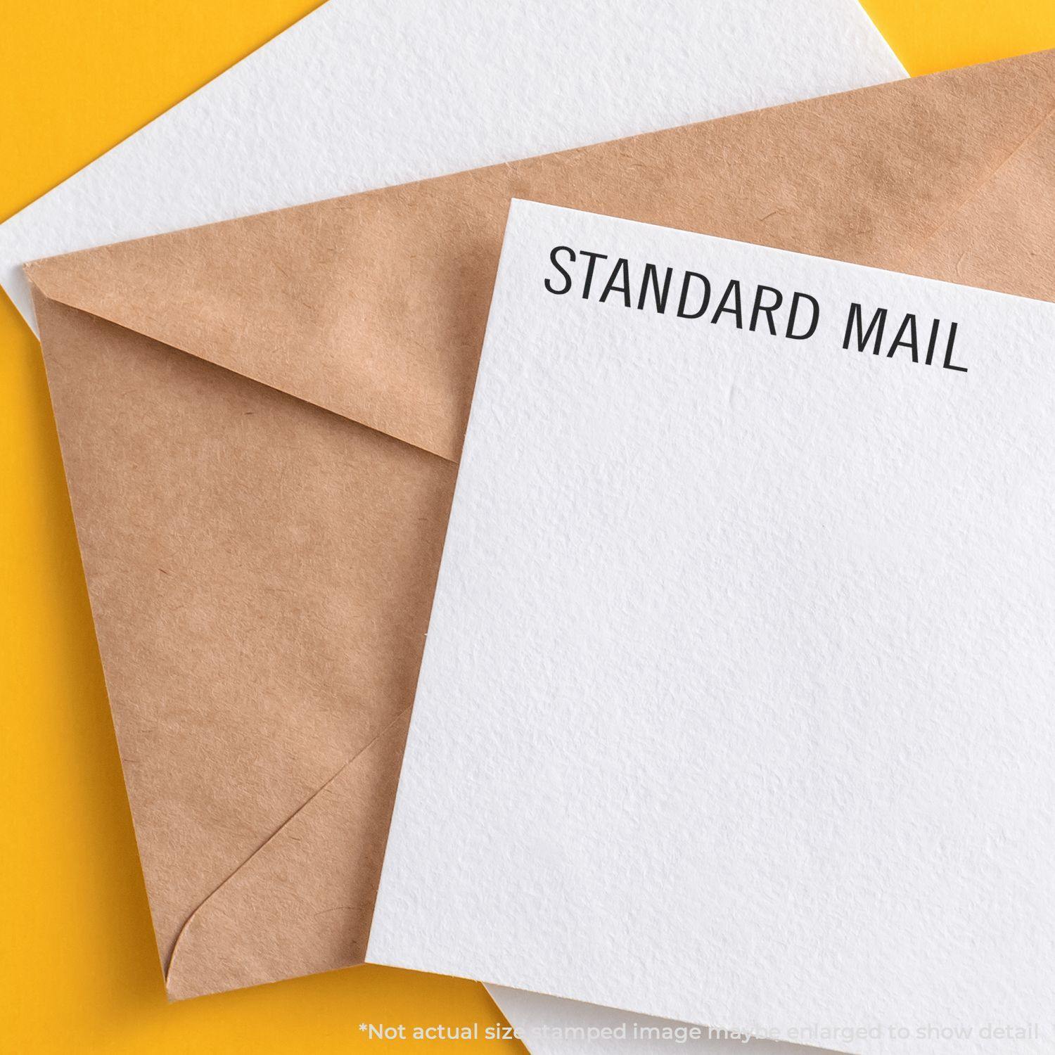 Slim Pre-Inked Standard Mail Stamp used on a white envelope next to a brown envelope on a yellow background.