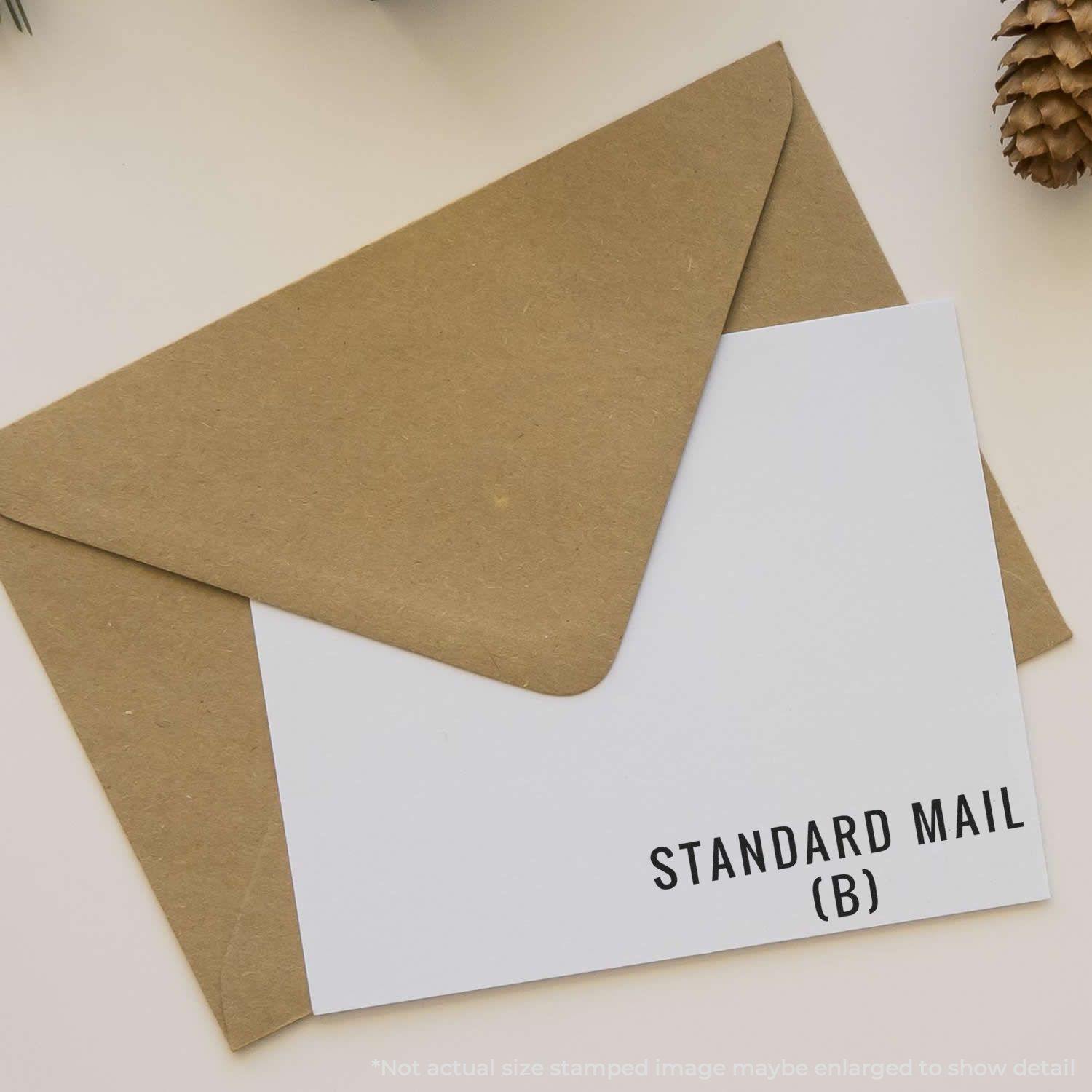 Standard Mail (B) rubber stamp on white card, placed on a brown envelope with a pine cone in the background.