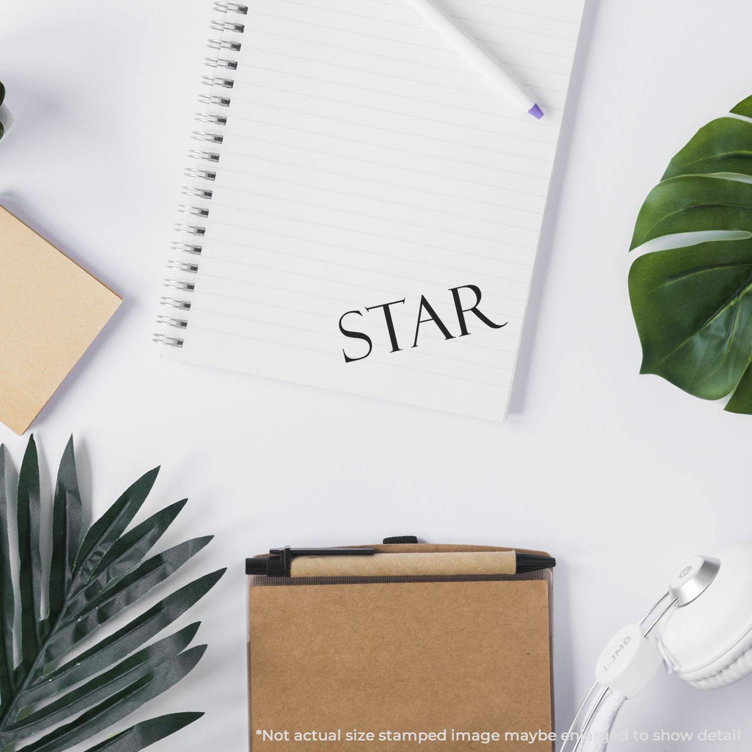 Large Pre-Inked Star Stamp used on a notebook, surrounded by plants, a pen, and a small box on a white desk.