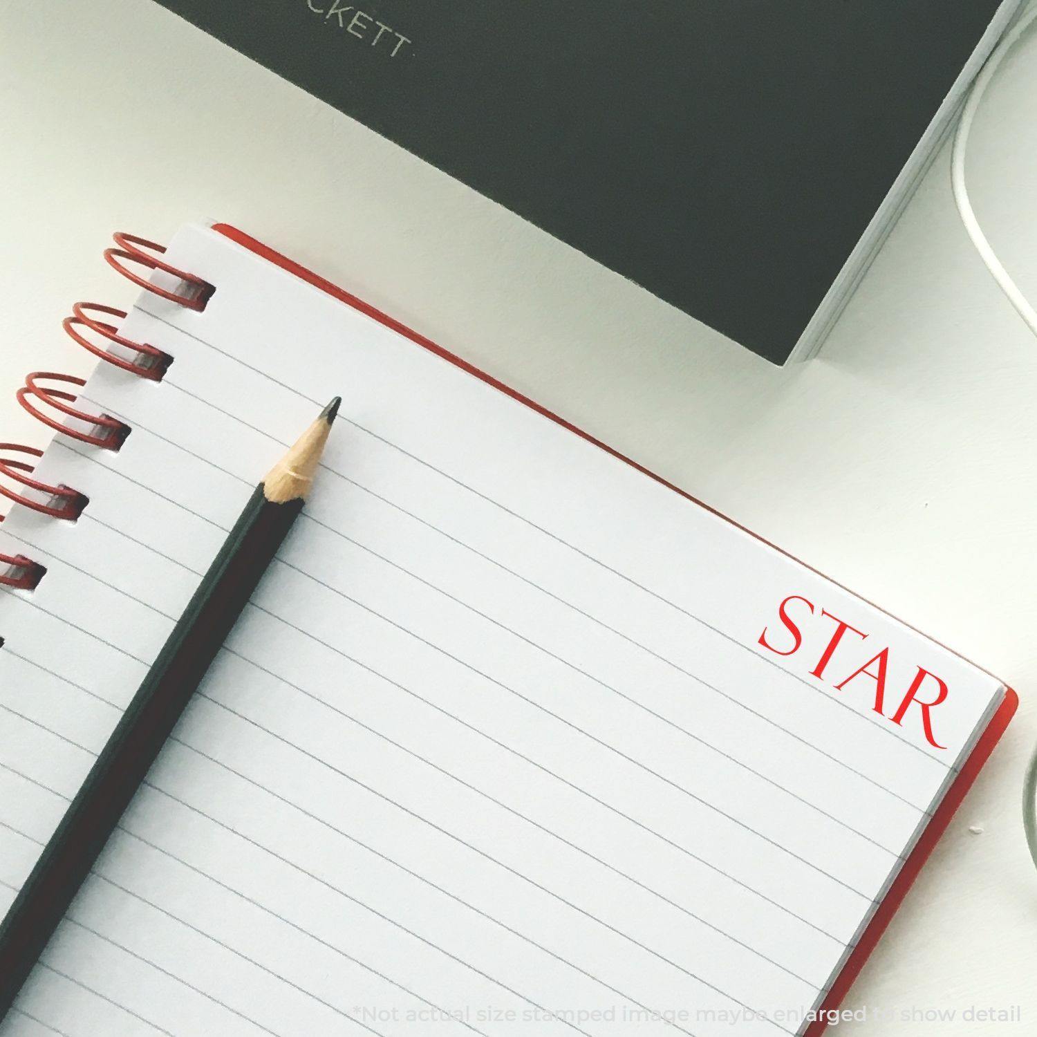 Large Pre-Inked Star Stamp used on a lined notebook with a pencil beside it, showing a red star stamp impression on the top right corner.