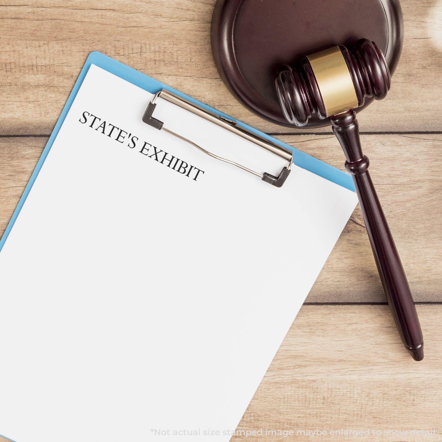 A Self Inking State's Exhibit Stamp is used on a document placed on a clipboard next to a gavel on a wooden desk.