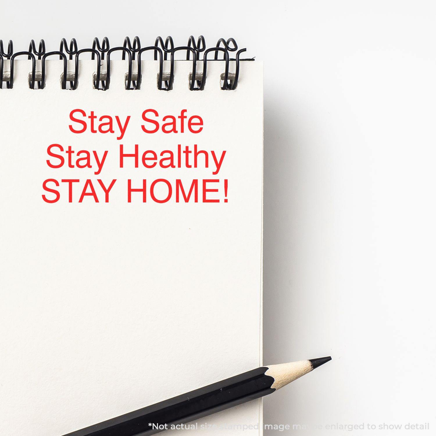 A notebook stamped with Stay Safe Stay Healthy STAY HOME! in red ink using the Self Inking Stay Safe Stay Healthy Stamp, with a pencil beside it.