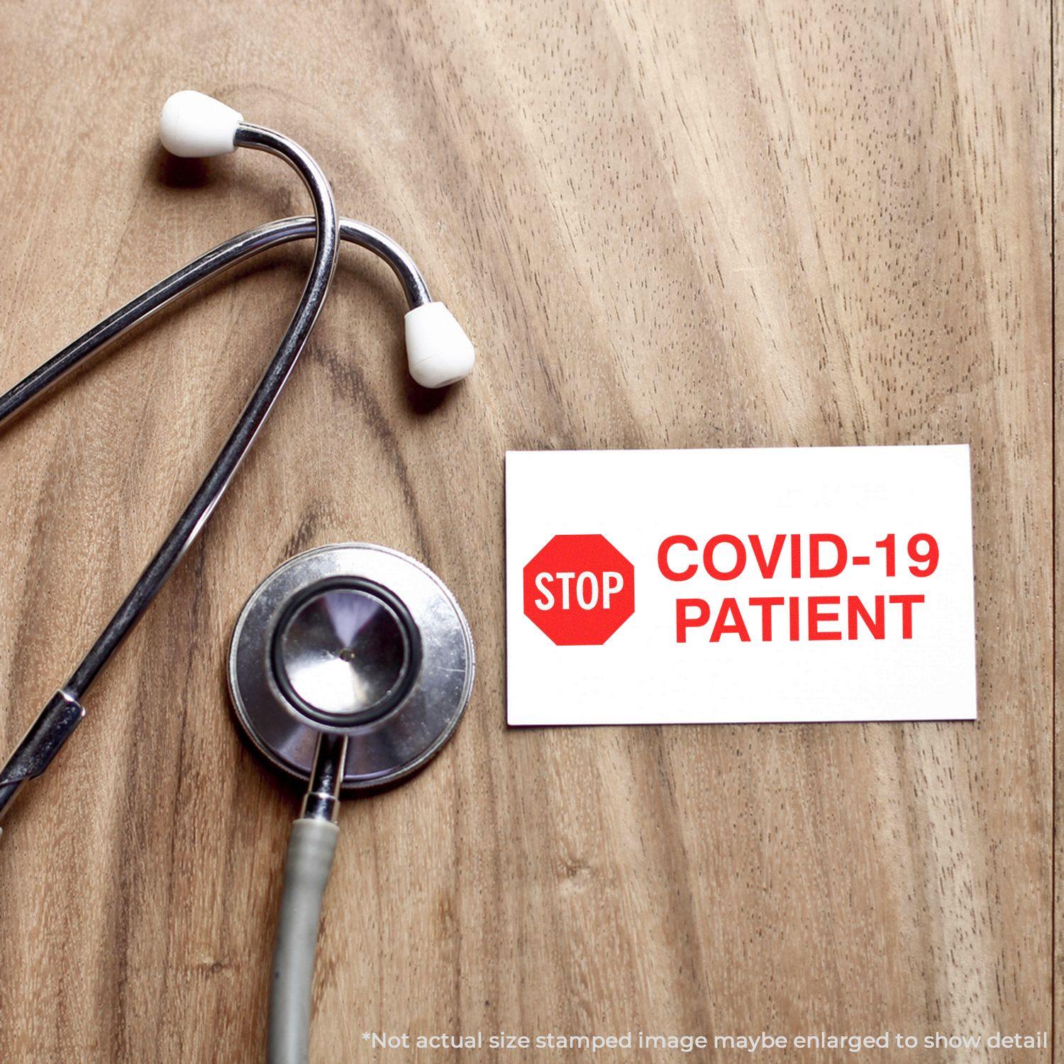 Stethoscope on a wooden surface next to a card stamped with STOP COVID-19 PATIENT using the Large Self Inking Stop Covid Patient Stamp.