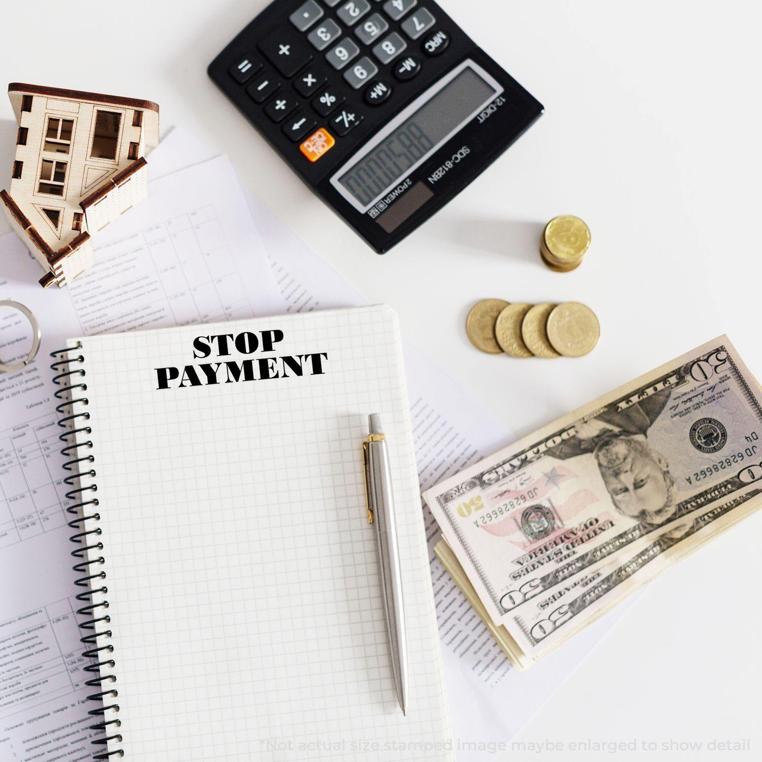 Large Self Inking Stop Payment Stamp used on a notebook, surrounded by a calculator, coins, dollar bills, and documents on a desk.