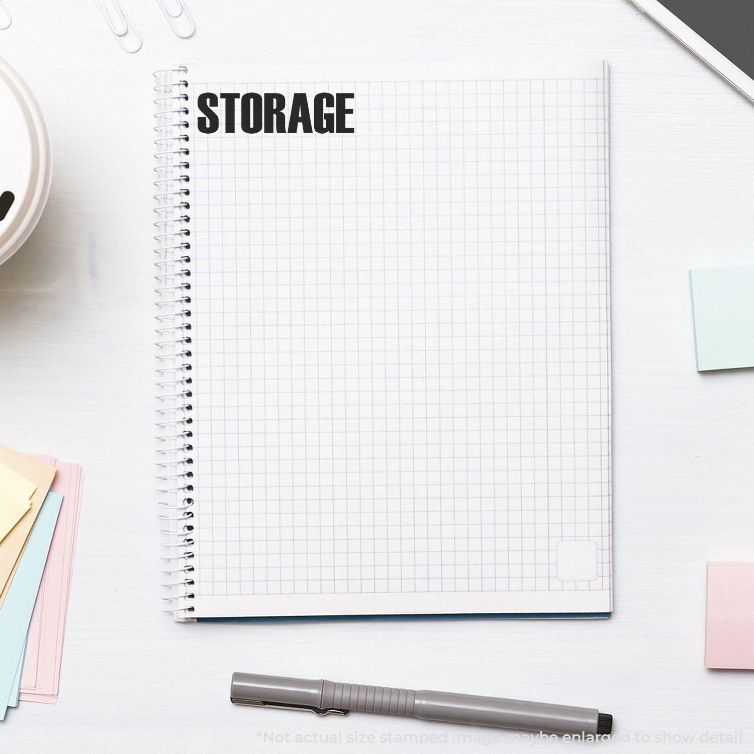 Slim Pre-Inked Storage Stamp used on a spiral notebook with a grid pattern, surrounded by office supplies on a white desk.