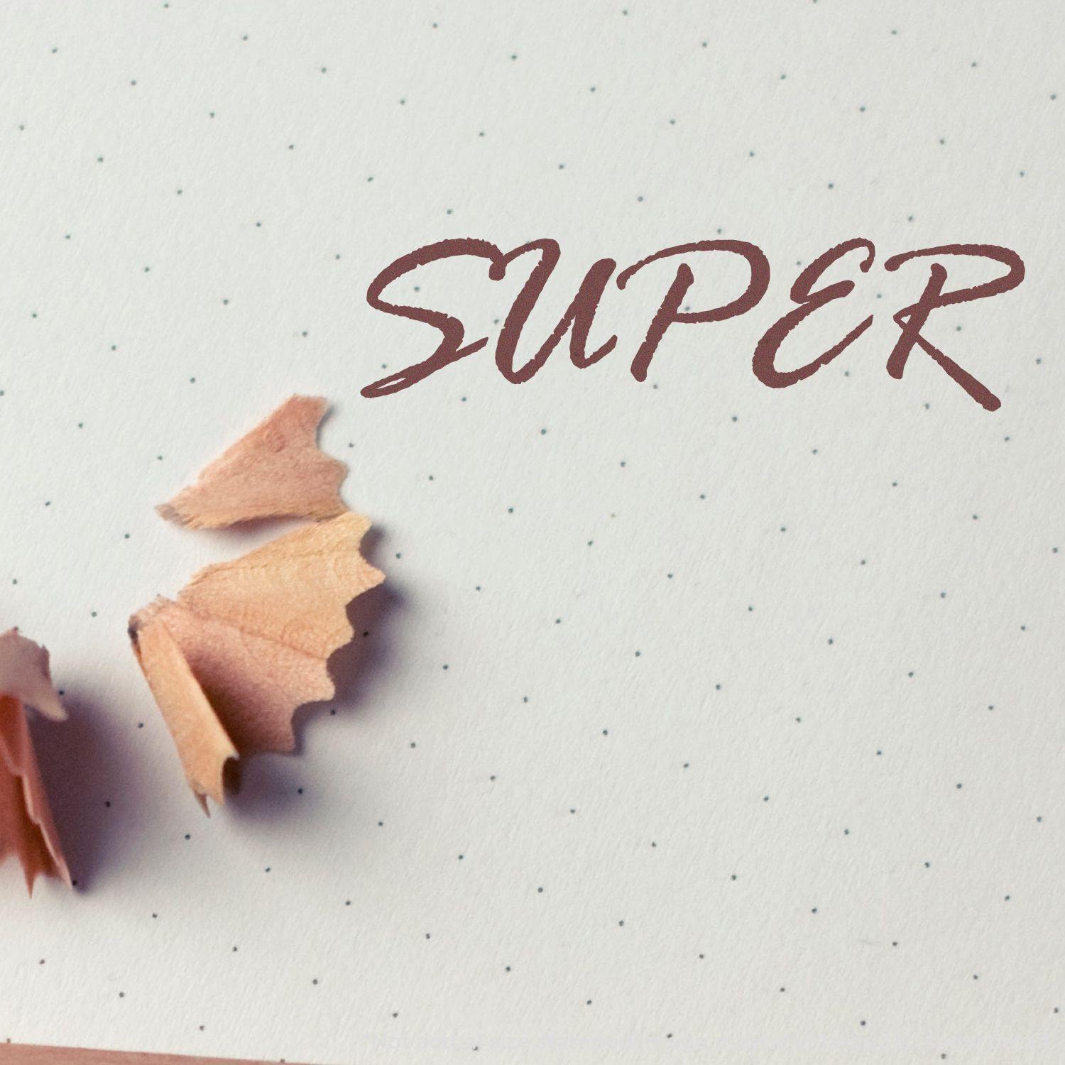 Large Pre-Inked Super Stamp imprinting the word SUPER on dotted paper, surrounded by pencil shavings.