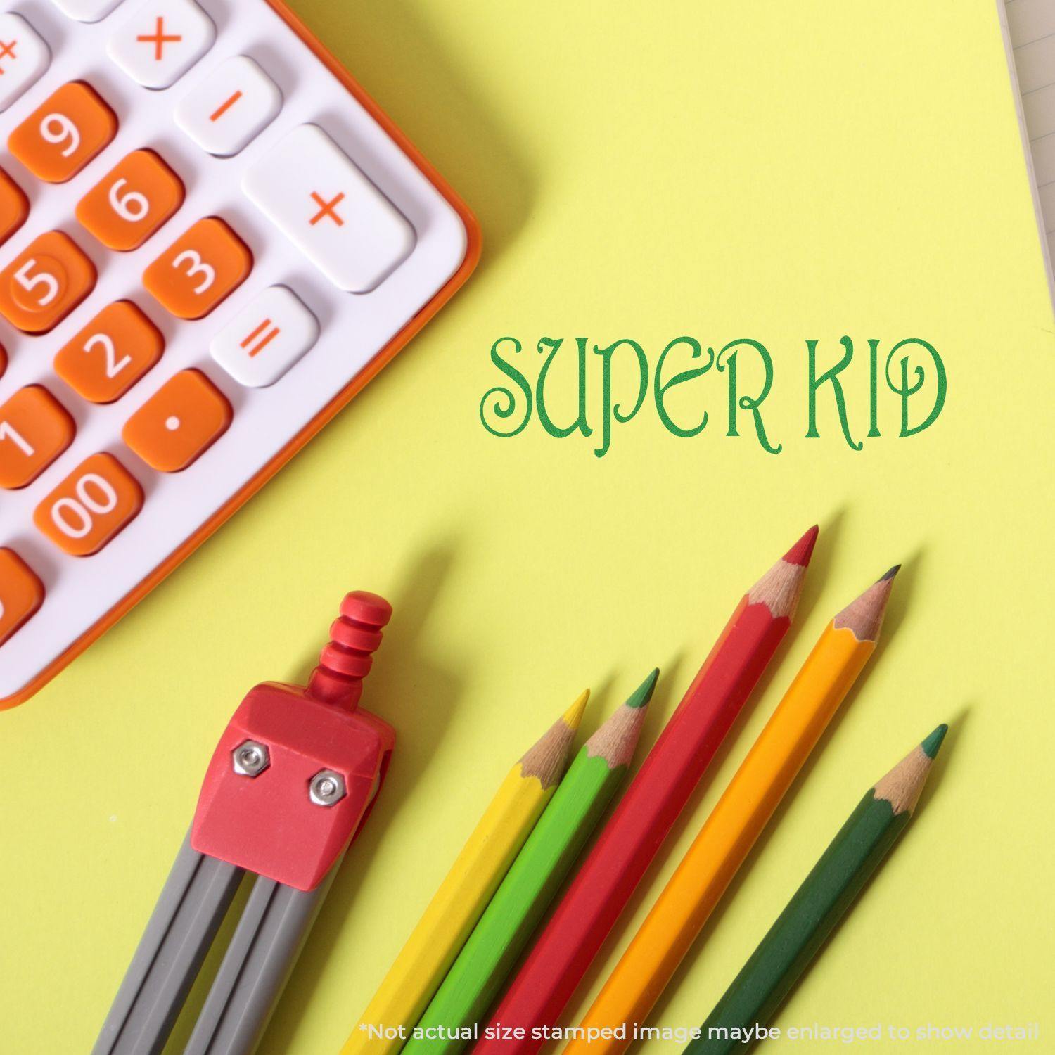 Large Pre-Inked Super Kid Stamp on yellow paper with colorful pencils, a robot eraser, and part of a calculator in the background.