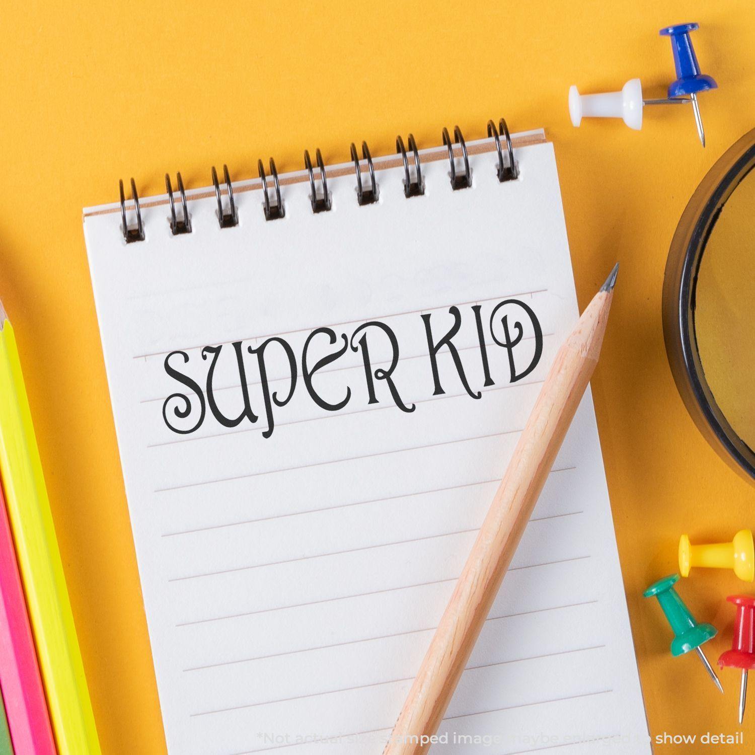 A notebook with SUPER KID stamped using the Self Inking Super Kid Stamp, surrounded by colorful pencils, push pins, and a magnifying glass.