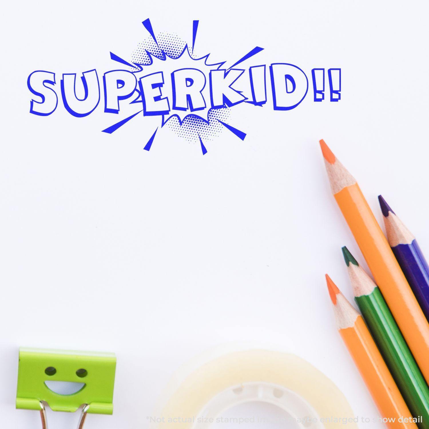 Slim Pre-Inked Superkid Stamp in blue ink on white paper, surrounded by colorful pencils, a smiling clip, and tape.