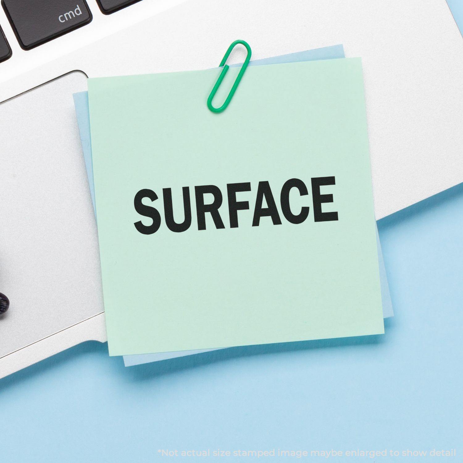 Self Inking Surface Stamp used on a green sticky note attached to a laptop keyboard with a green paperclip.