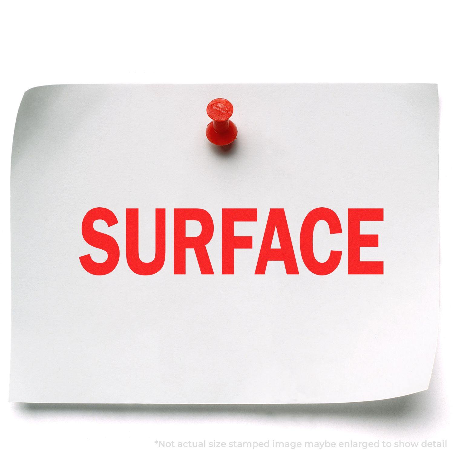 A white paper with the word SURFACE stamped in red using a Self Inking Surface Stamp, pinned to a white background with a red pushpin.