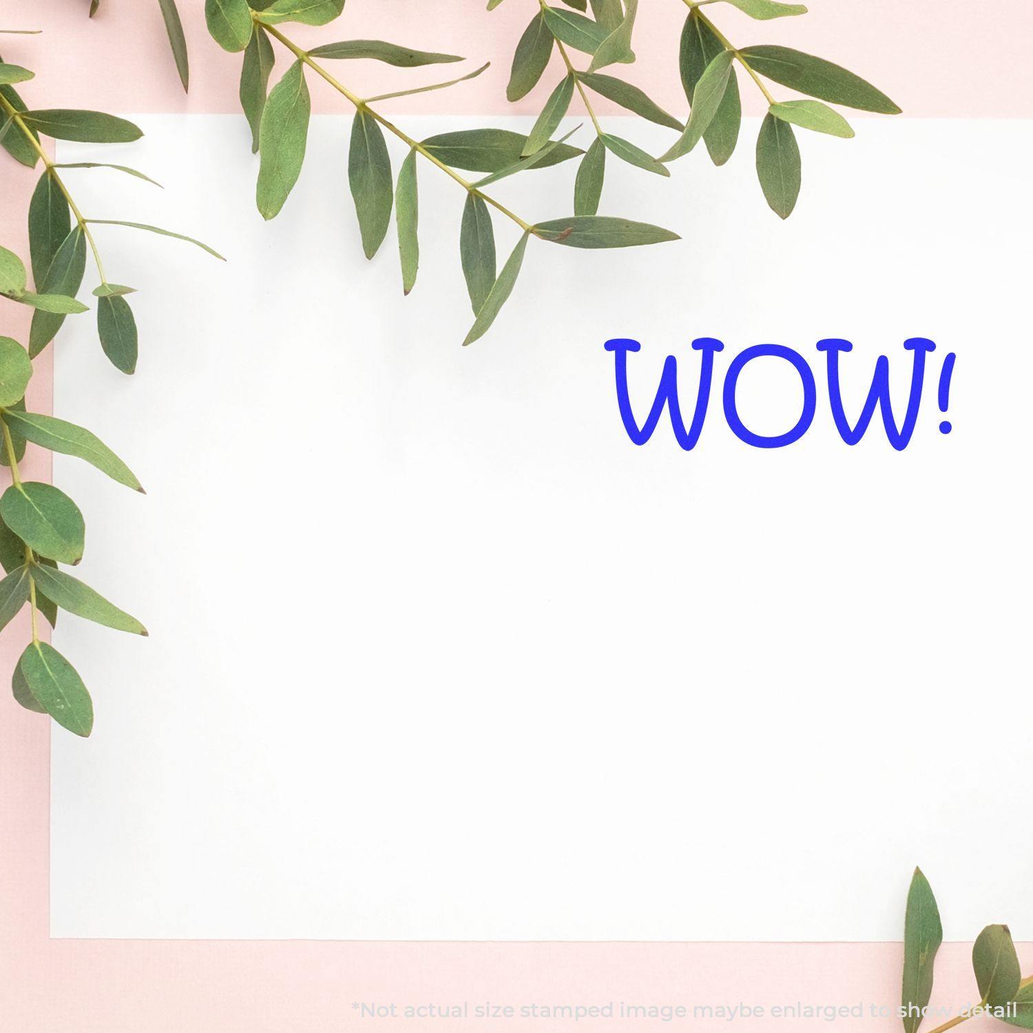 White paper with 'WOW!' stamped in blue using a Slim Pre-Inked WOW Stamp, surrounded by green leaves on a light pink background.