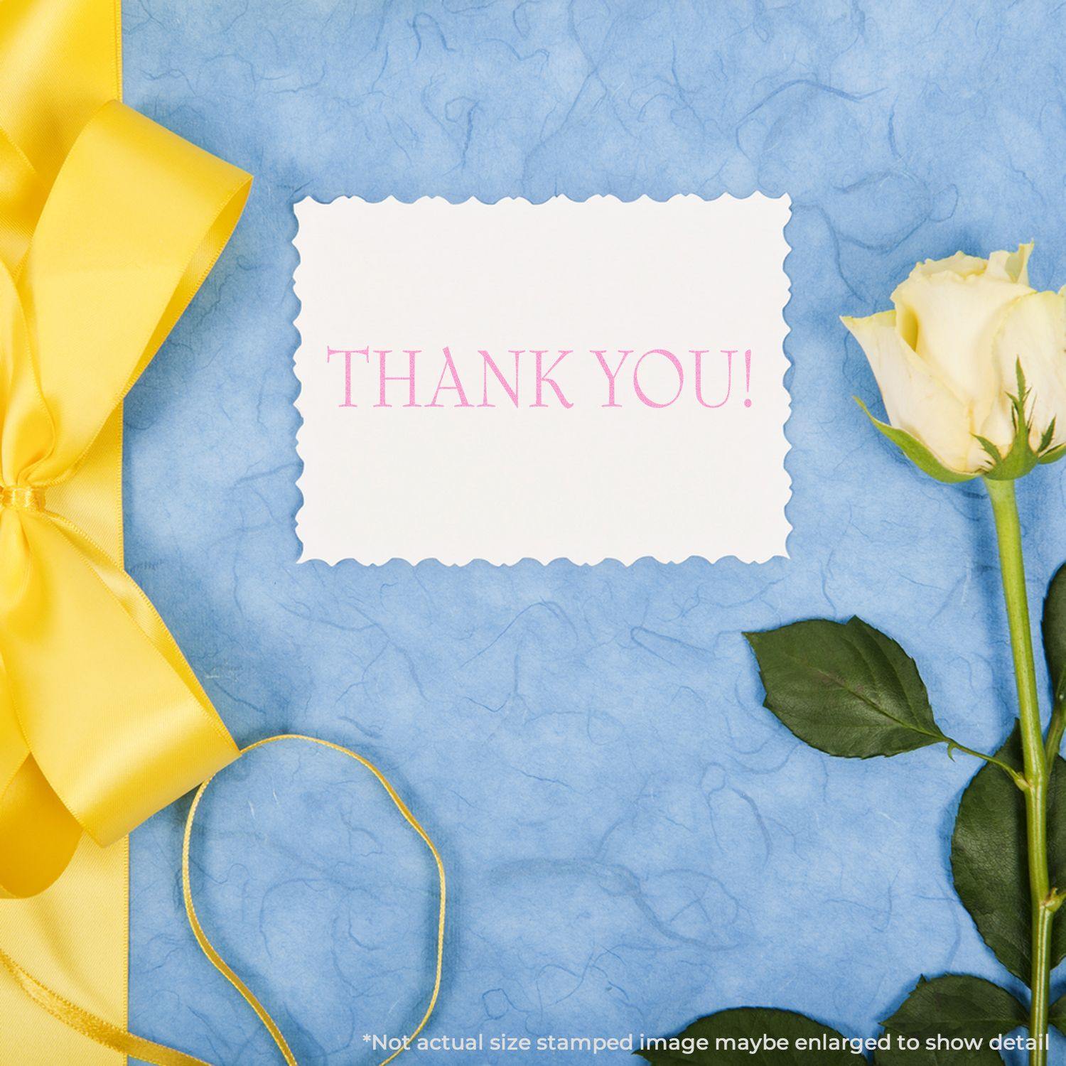 A Large Self Inking Thank You Stamp on a white card with a yellow ribbon and rose on a blue textured background.