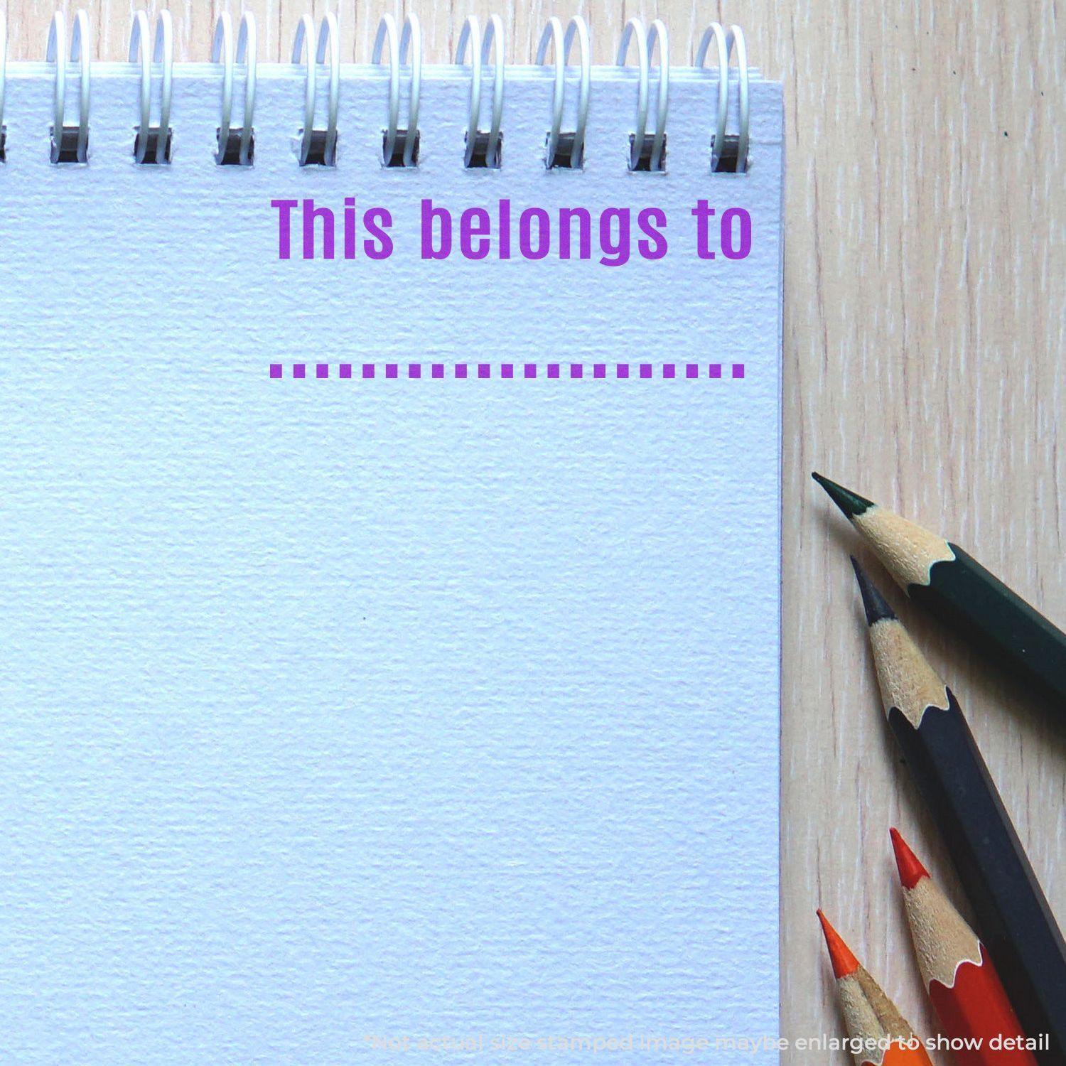 A notebook with This belongs to stamped on the page using a Self Inking This belongs to ... Stamp, with colored pencils beside it.