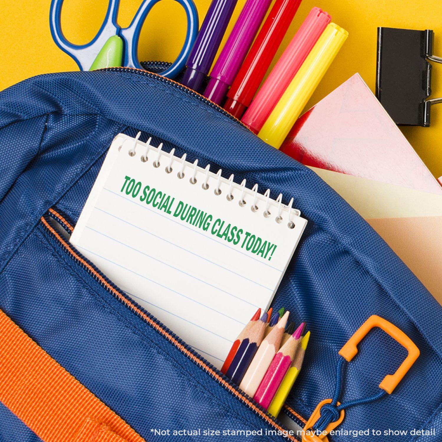 A Large Self-Inking Too Social During Class Today Stamp is used on a notepad placed in a blue backpack with school supplies.