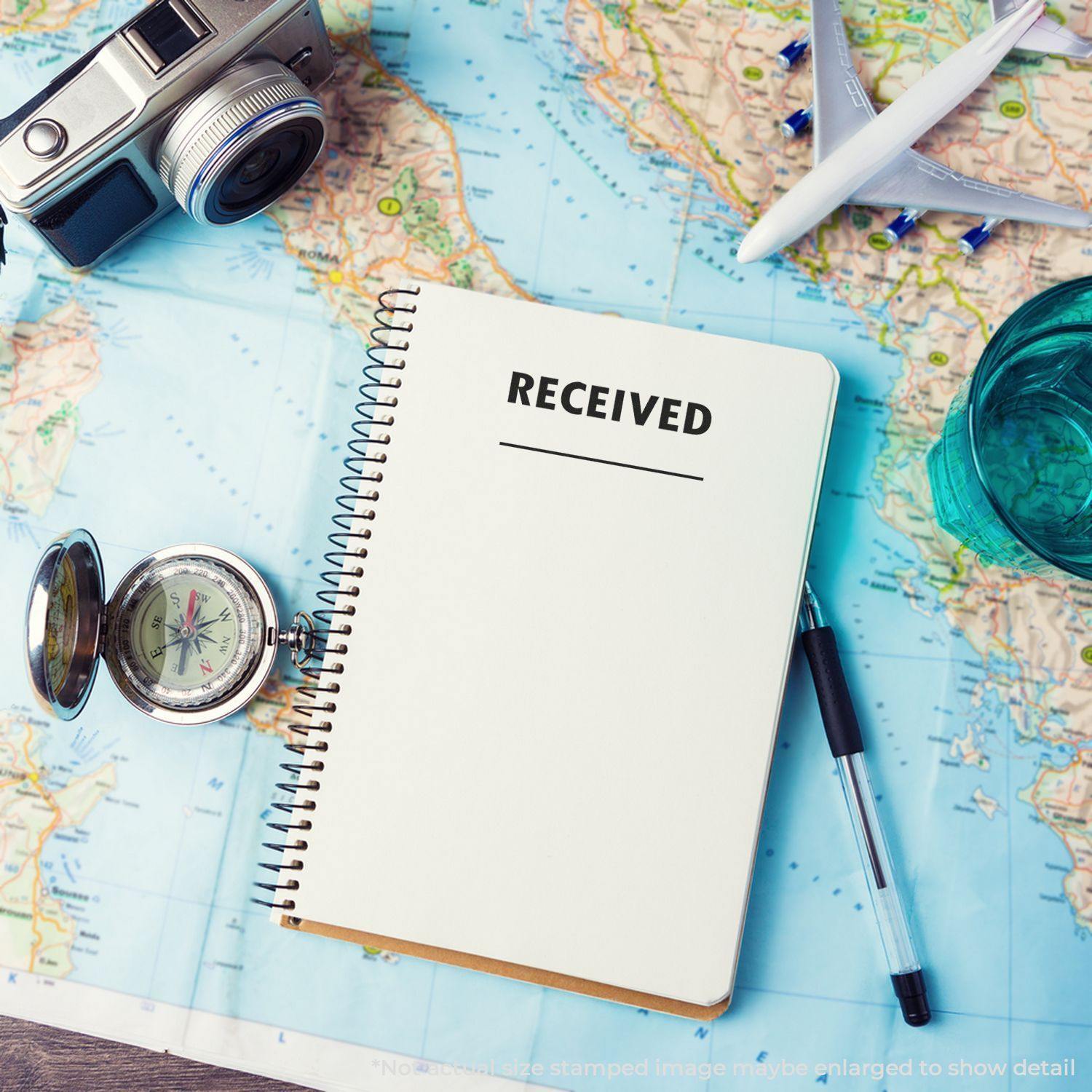 Notebook with RECEIVED stamped using a Two Line Received Rubber Stamp, placed on a world map with a camera, compass, and pen.