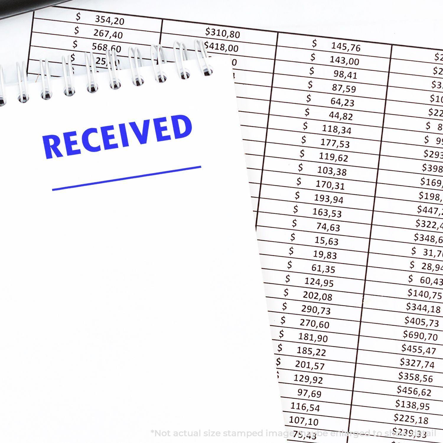 Large Self Inking Two Line Received Stamp marking RECEIVED in blue ink on a notepad, with financial documents in the background.