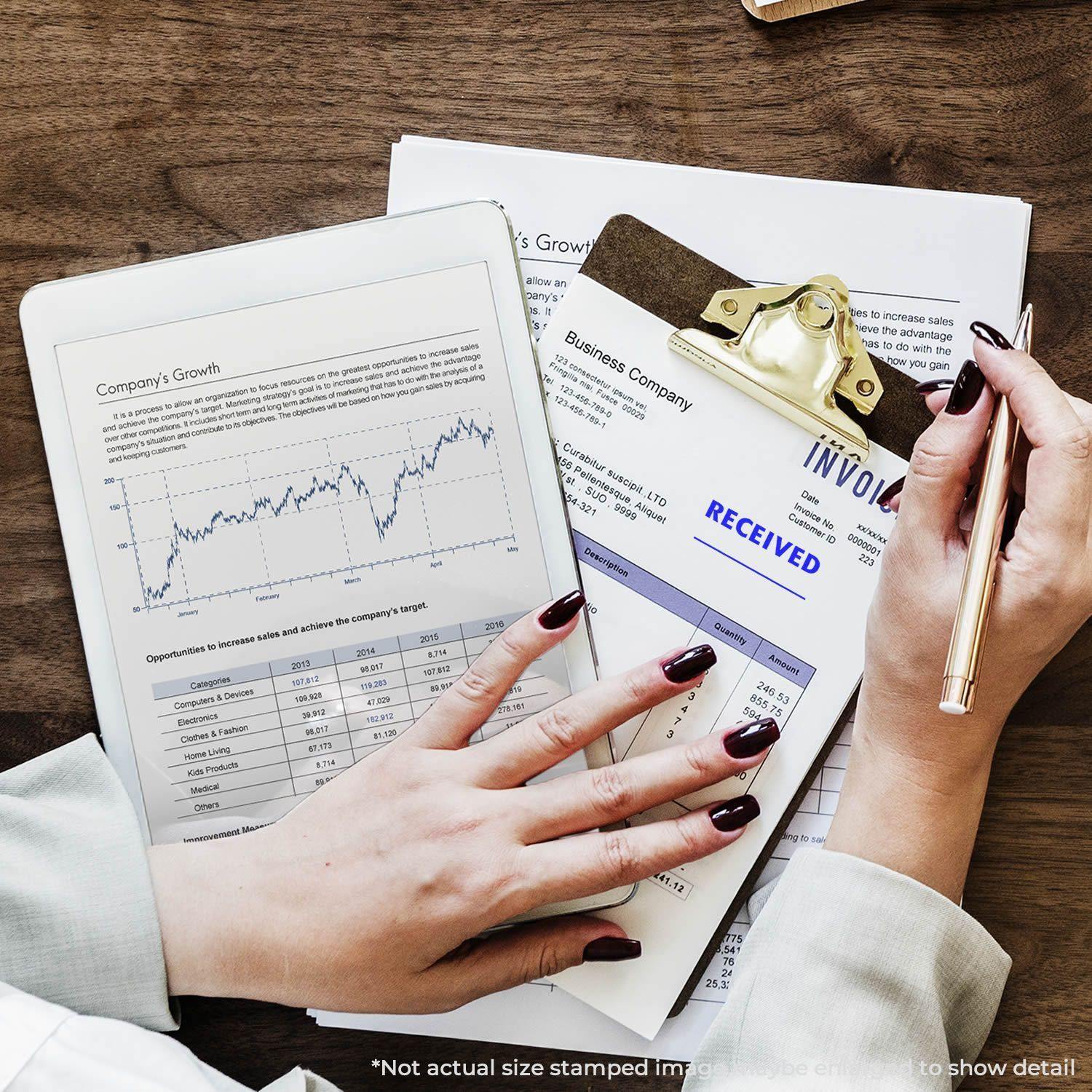 Person using Self Inking Two Line Received Stamp on an invoice, with a tablet displaying a graph and a clipboard with documents.