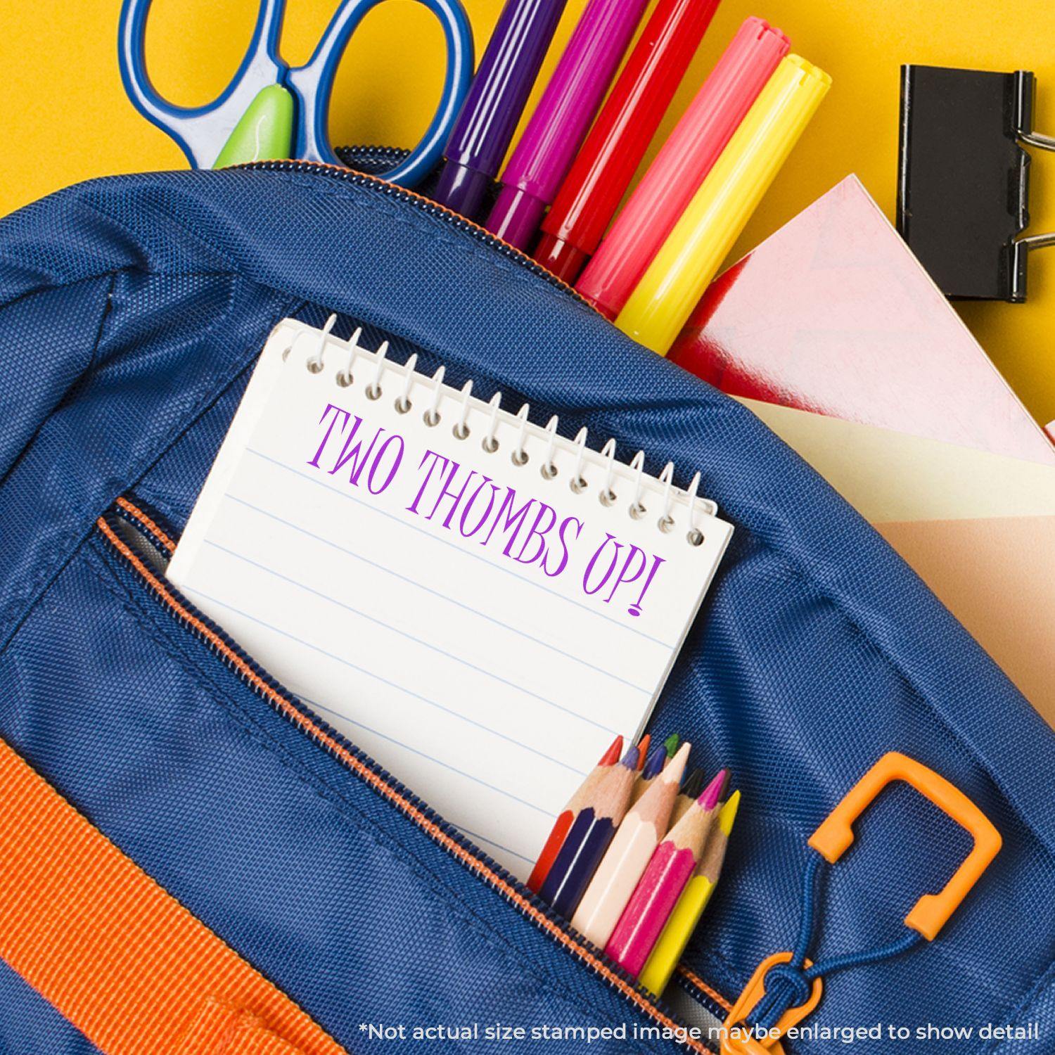 A Slim Pre-Inked Two Thumbs Up Stamp is used on a notepad inside a blue backpack with colorful stationery items around it.