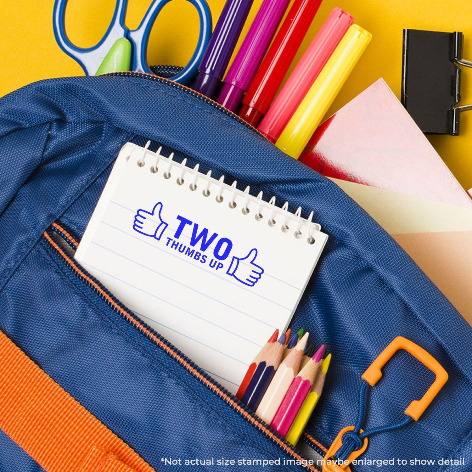 Large Pre-Inked Two Thumbs Up with Thumb Icon Stamp used on a notepad, surrounded by school supplies in a blue backpack.