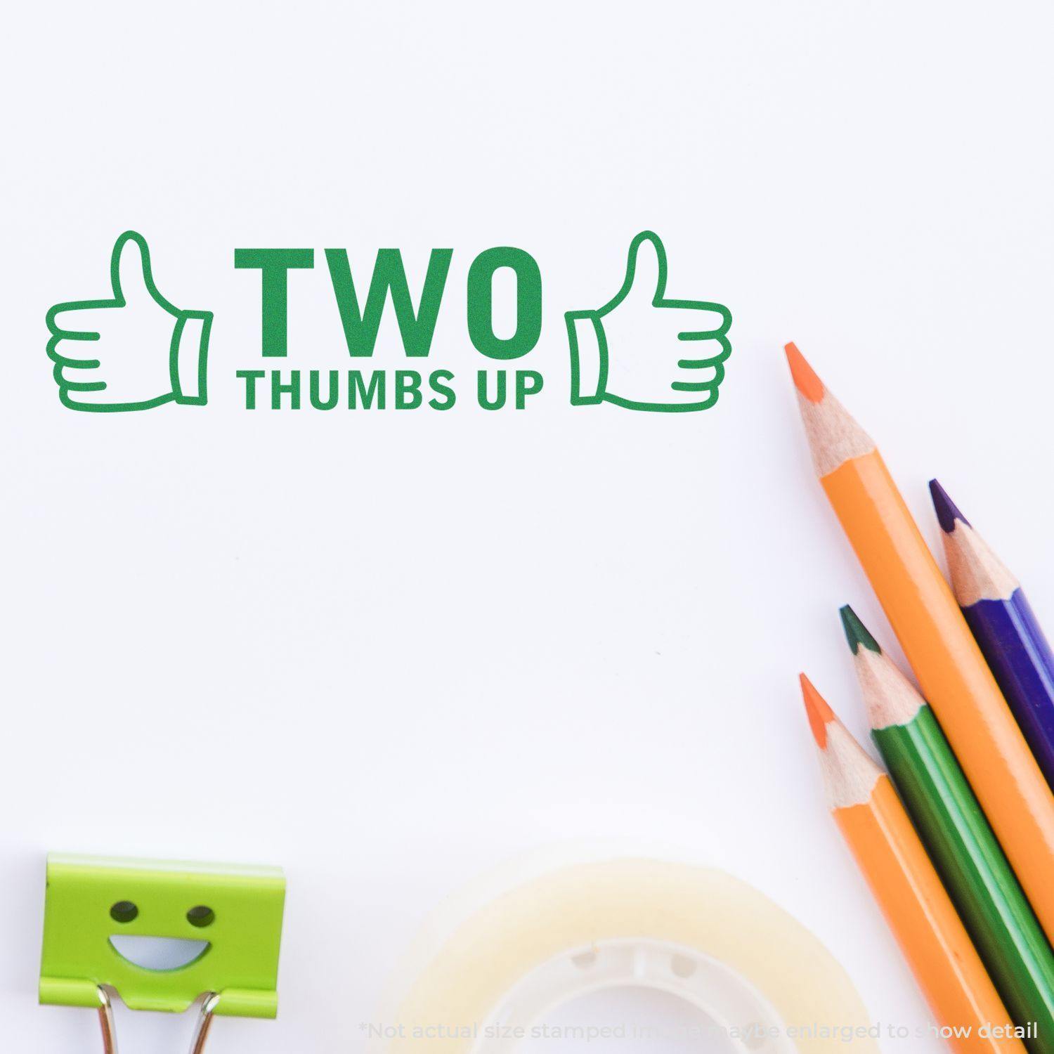 Two Thumbs Up with Thumb Icon Rubber Stamp in green ink on white paper, surrounded by colorful pencils, tape, and a binder clip.