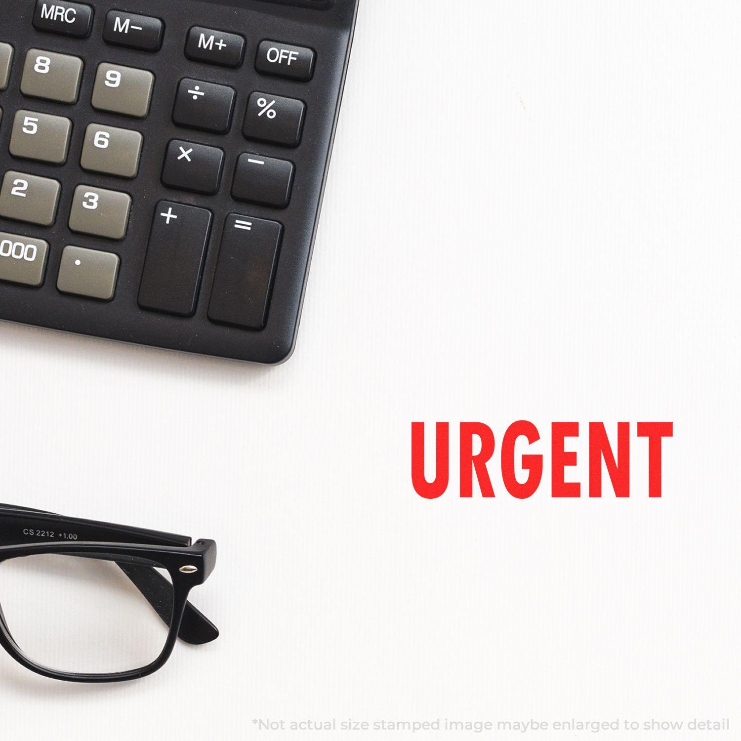 A Large Pre-Inked Urgent Stamp impression in red ink is shown on a white surface next to a calculator and a pair of black glasses.